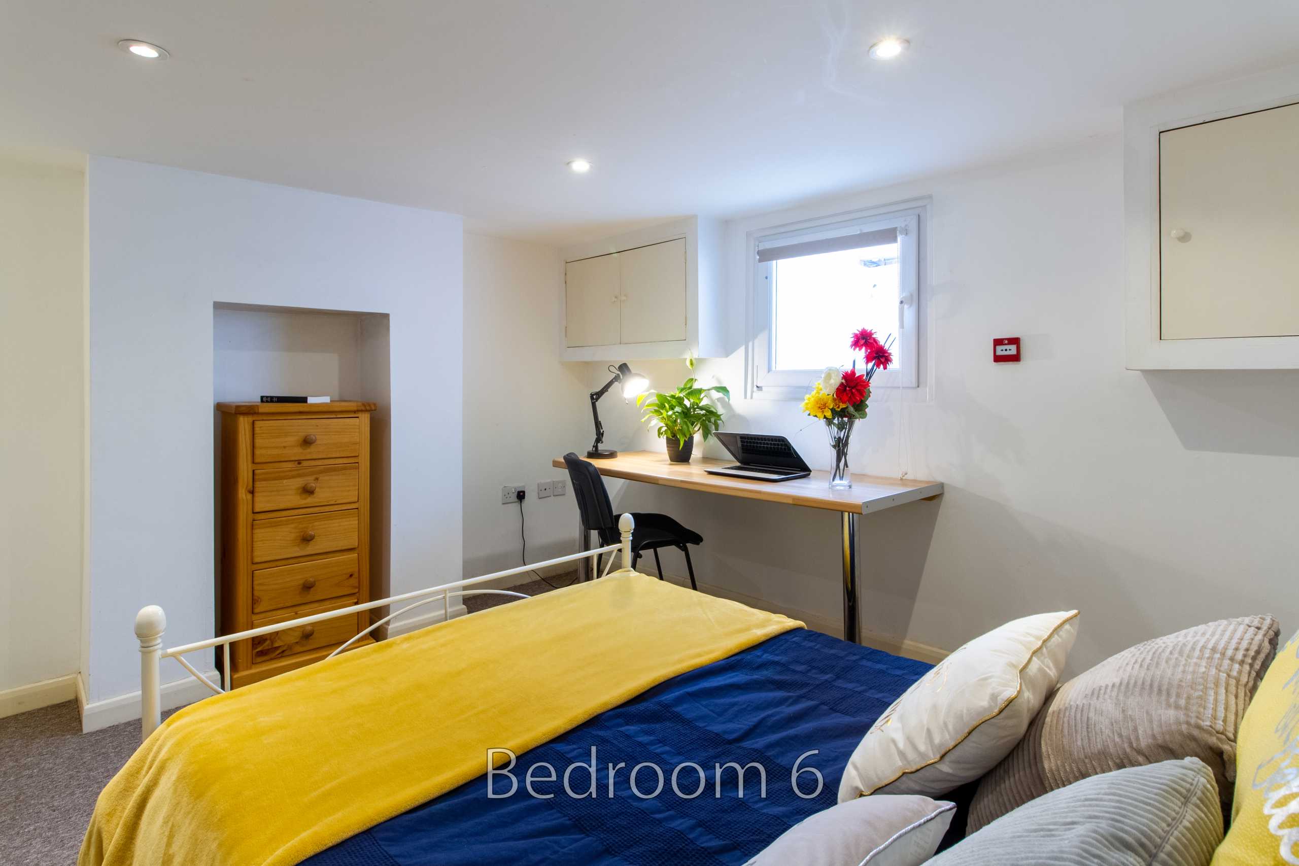 A bedroom with a bed, desk, chair, chest of drawers, and window.