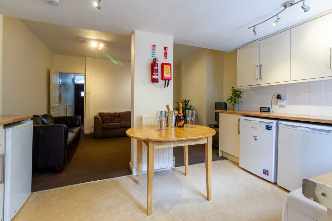 Open-plan communal kitchen and lounge area with a dining table, kitchenette, sofas and cupboards.