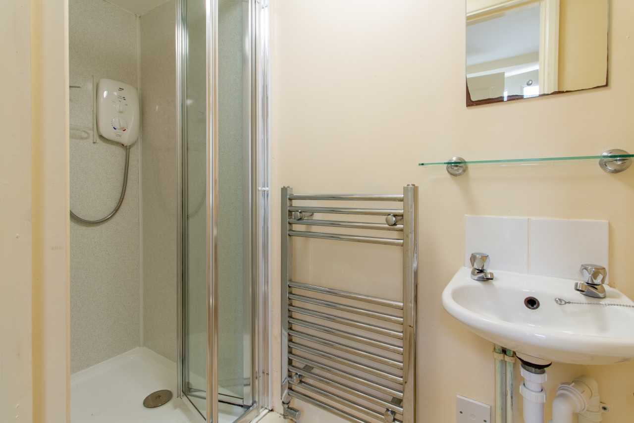 Bathroom with a shower enclosure, pedestal sink, heated towel rail and wall mirror.
