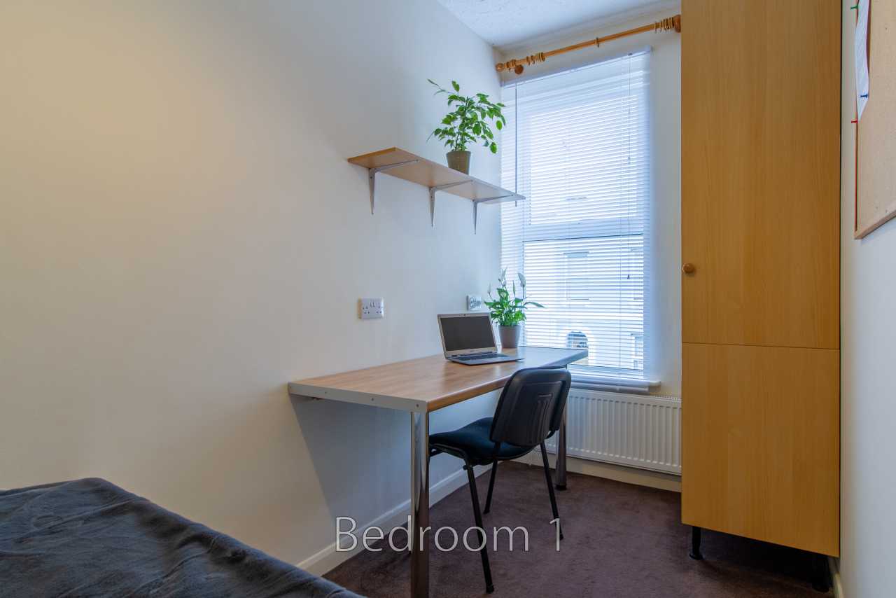 A bedroom with a single bed, desk, chair, wardrobe, shelves, window and radiator.