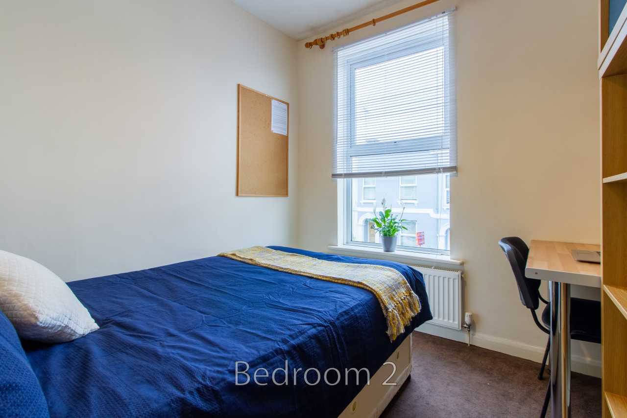 A bedroom with a double bed, window with blinds, desk and chair.