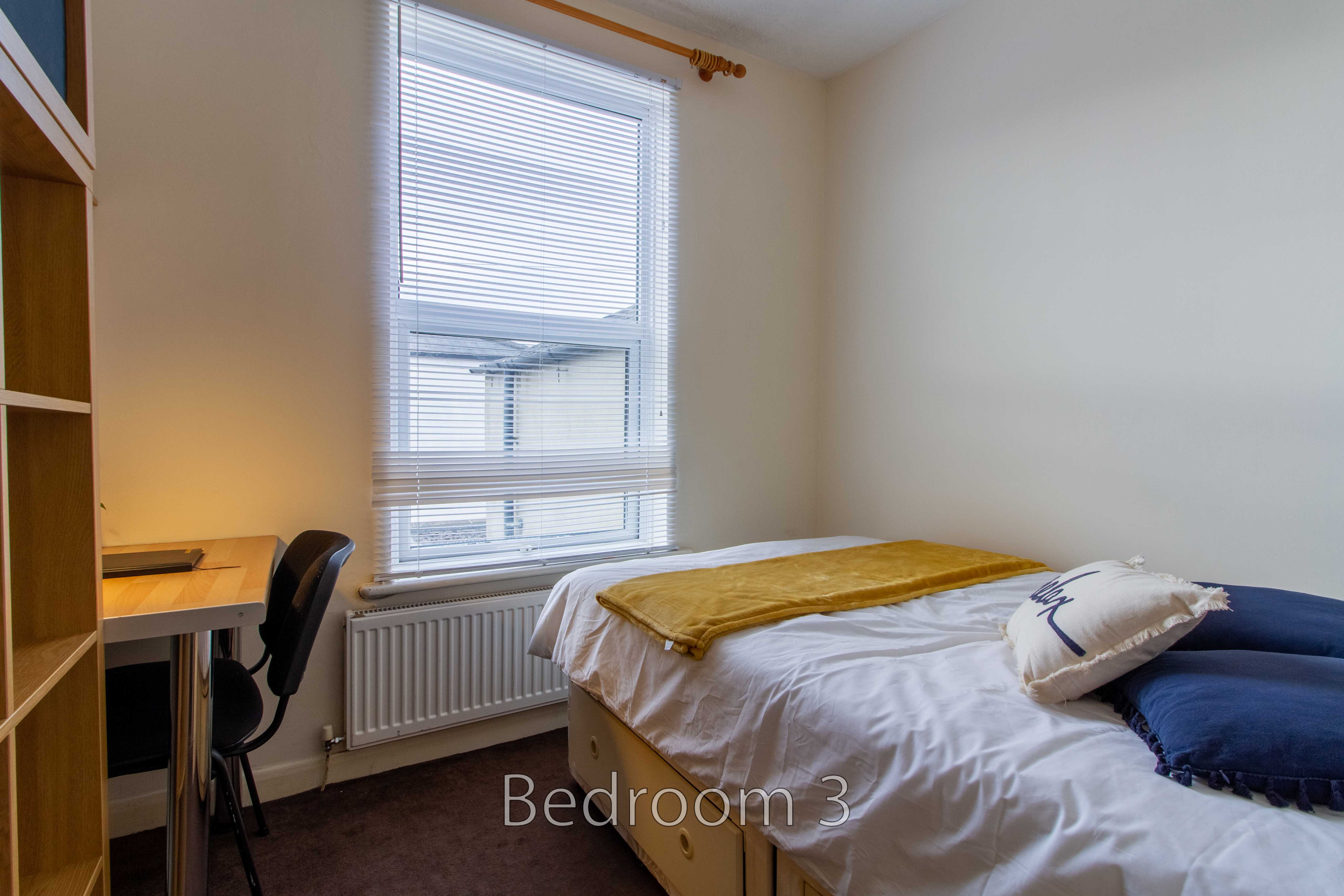 A bedroom with a single bed, desk, chair, window and radiator.
