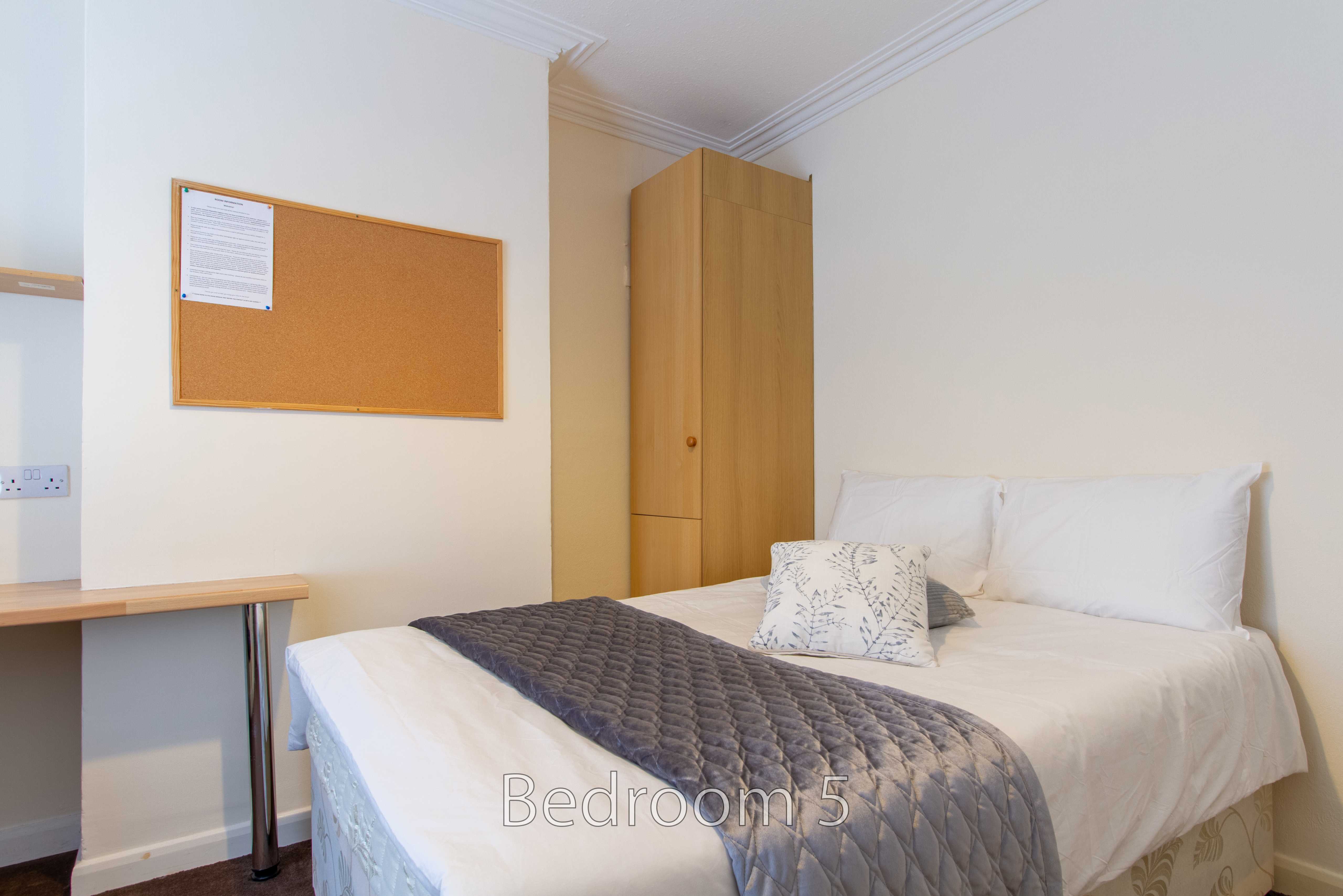 A furnished bedroom with a double bed, wardrobe, desk and noticeboard.