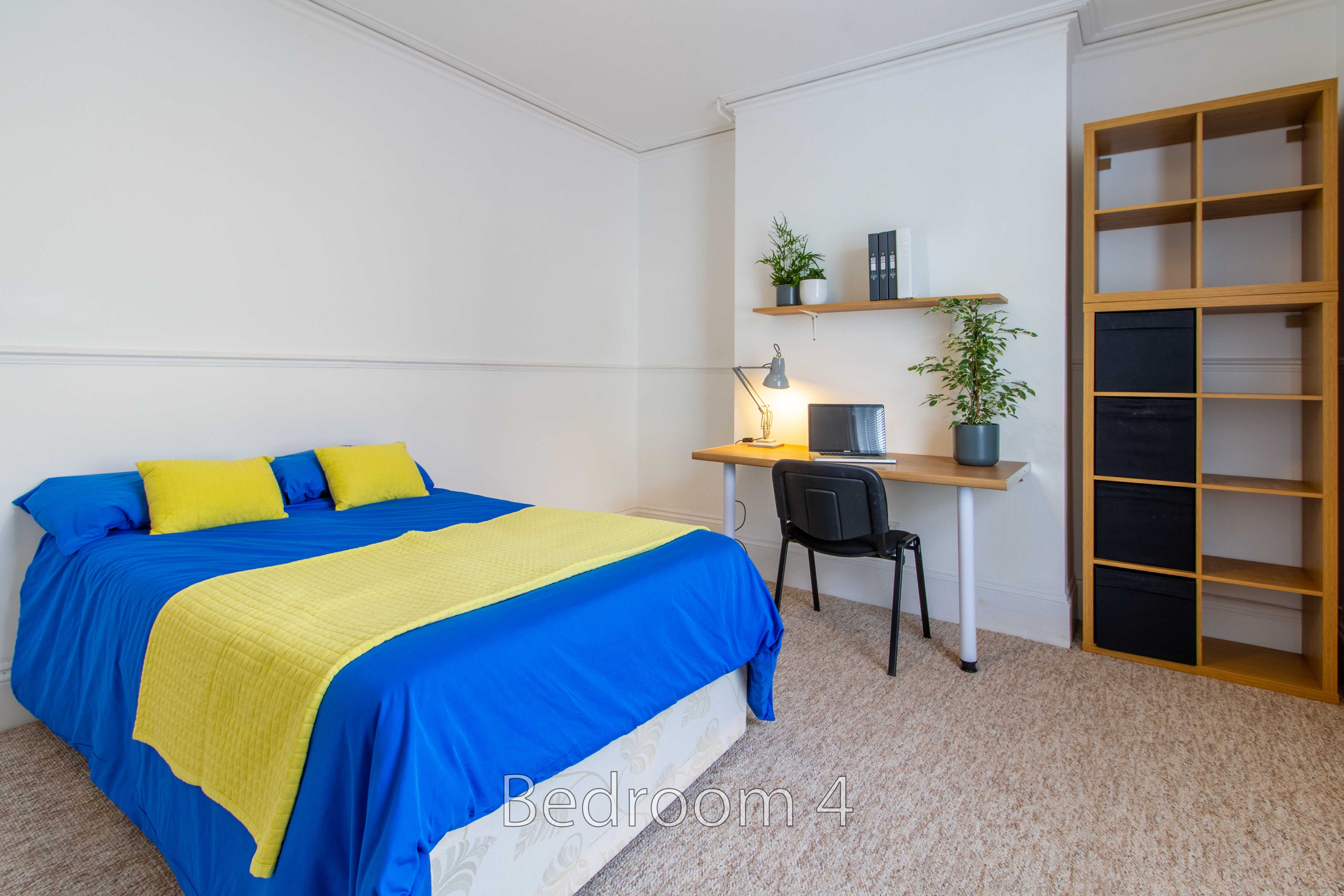 A bedroom with a blue and yellow bed, desk, chair, plants and built-in shelving.