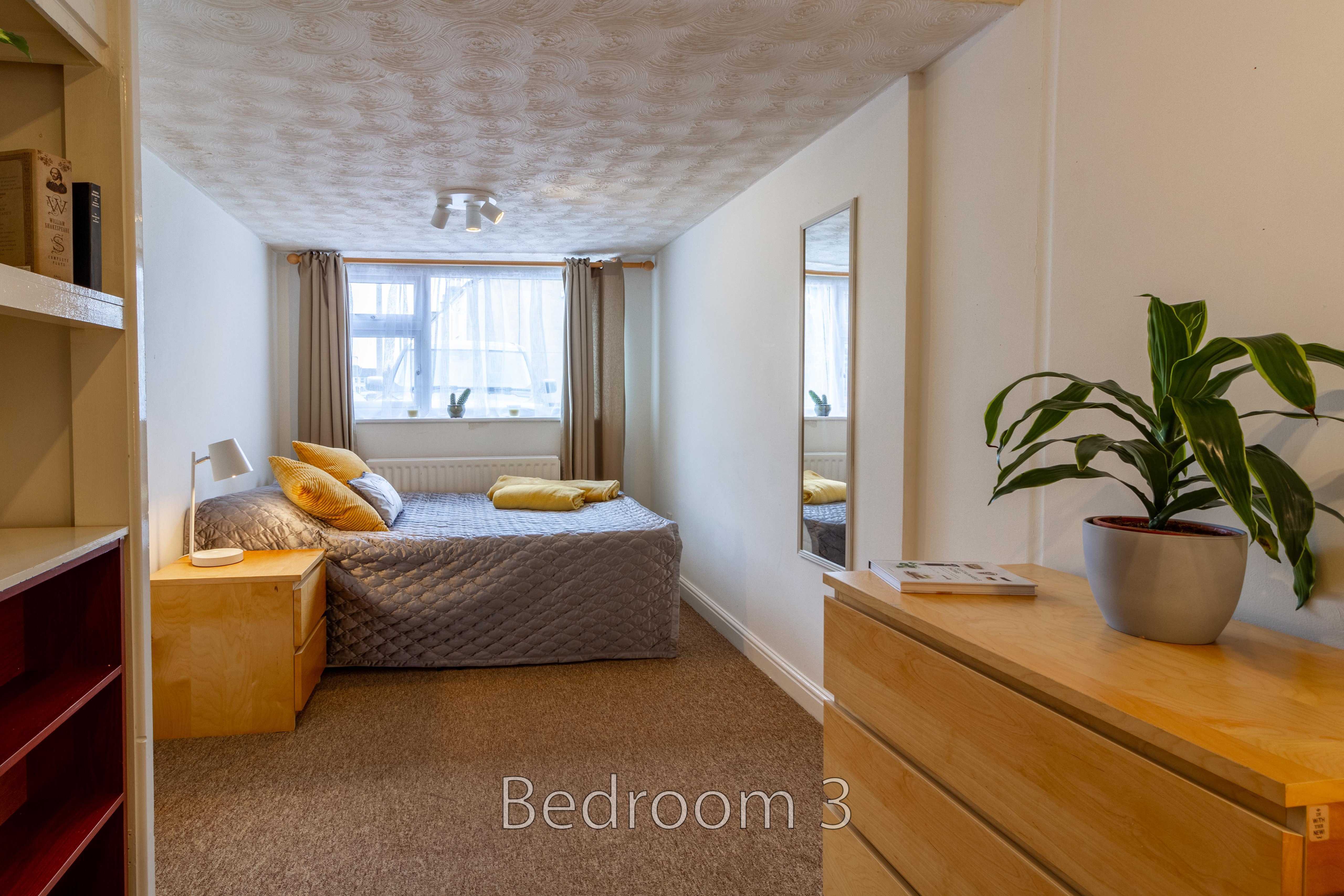 Furnished bedroom with a double bed, bedside table, chest of drawers, shelving, and a window.