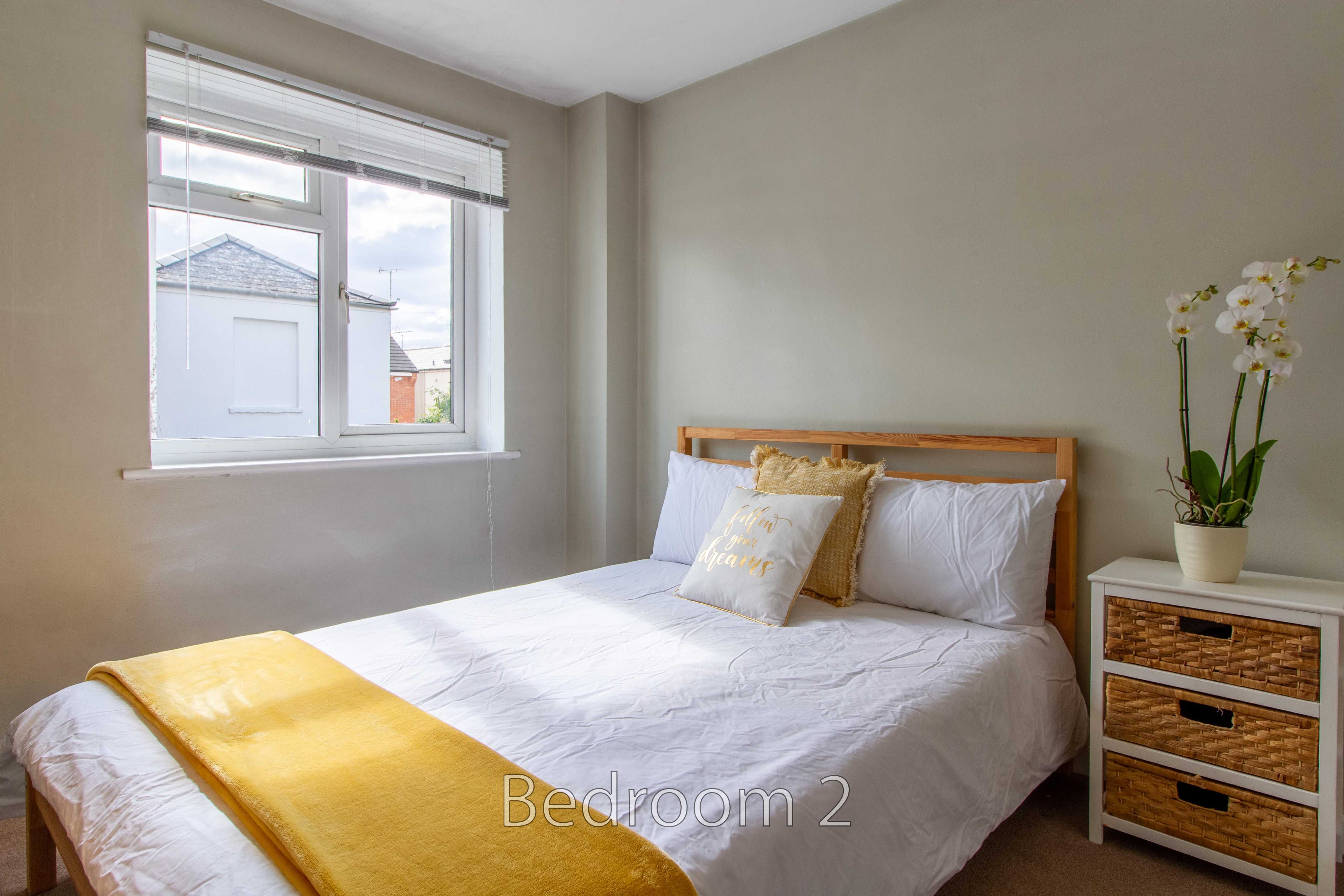 A furnished bedroom with a double bed, bedside chest, window and potted orchid.