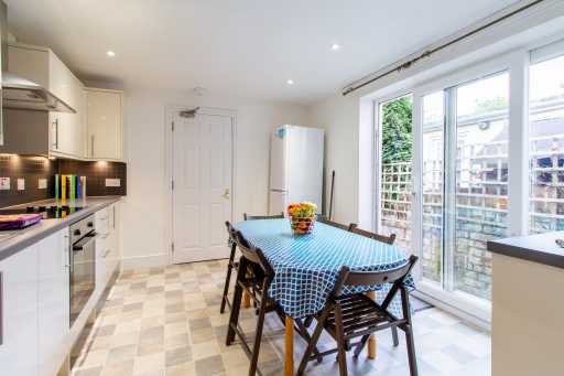 Bright kitchen and dining area with white cabinets, appliances, a table with chairs, and large glazed doors opening to a patio.