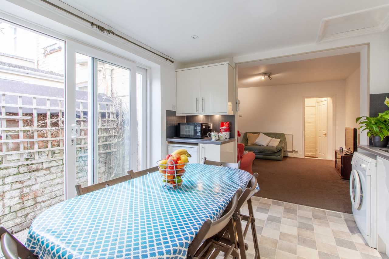 Open-plan kitchen and dining area with a table, chairs, appliances, and a visible adjoining living area.