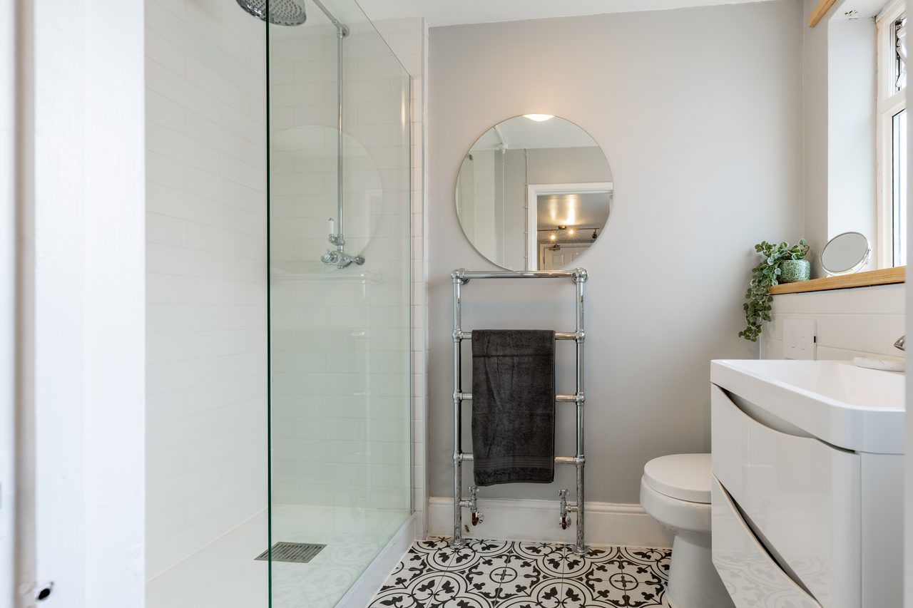 Bright modern bathroom with a glass walk-in shower, toilet, sink vanity, heated towel rail and patterned floor tiles.