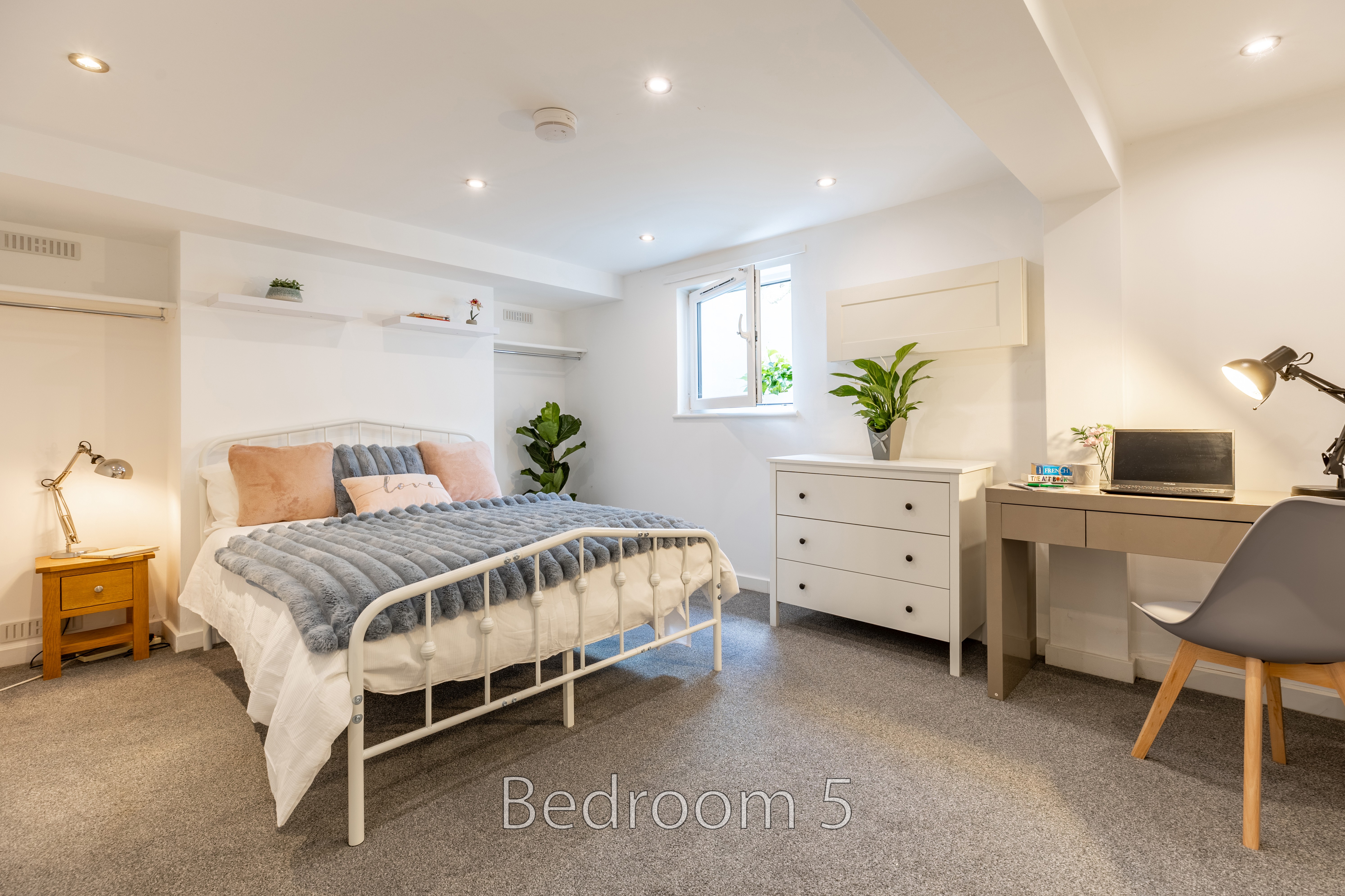 A furnished bedroom with a double bed, bedside table, dresser, desk and chair.