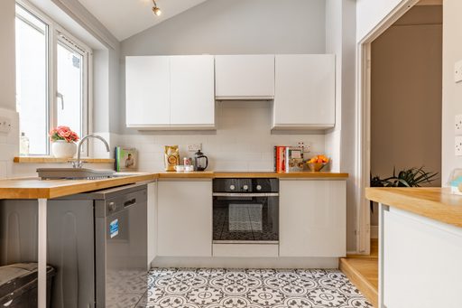 Bright modern kitchen with white cabinets, wood countertops, a sink, dishwasher, oven and patterned floor tiles.