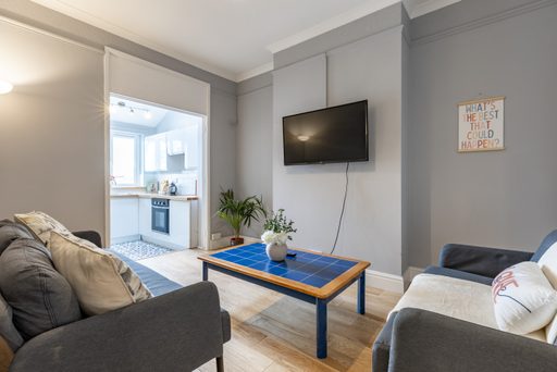 Furnished living room with sofas, a wall-mounted television, coffee table and open doorway to a kitchen.
