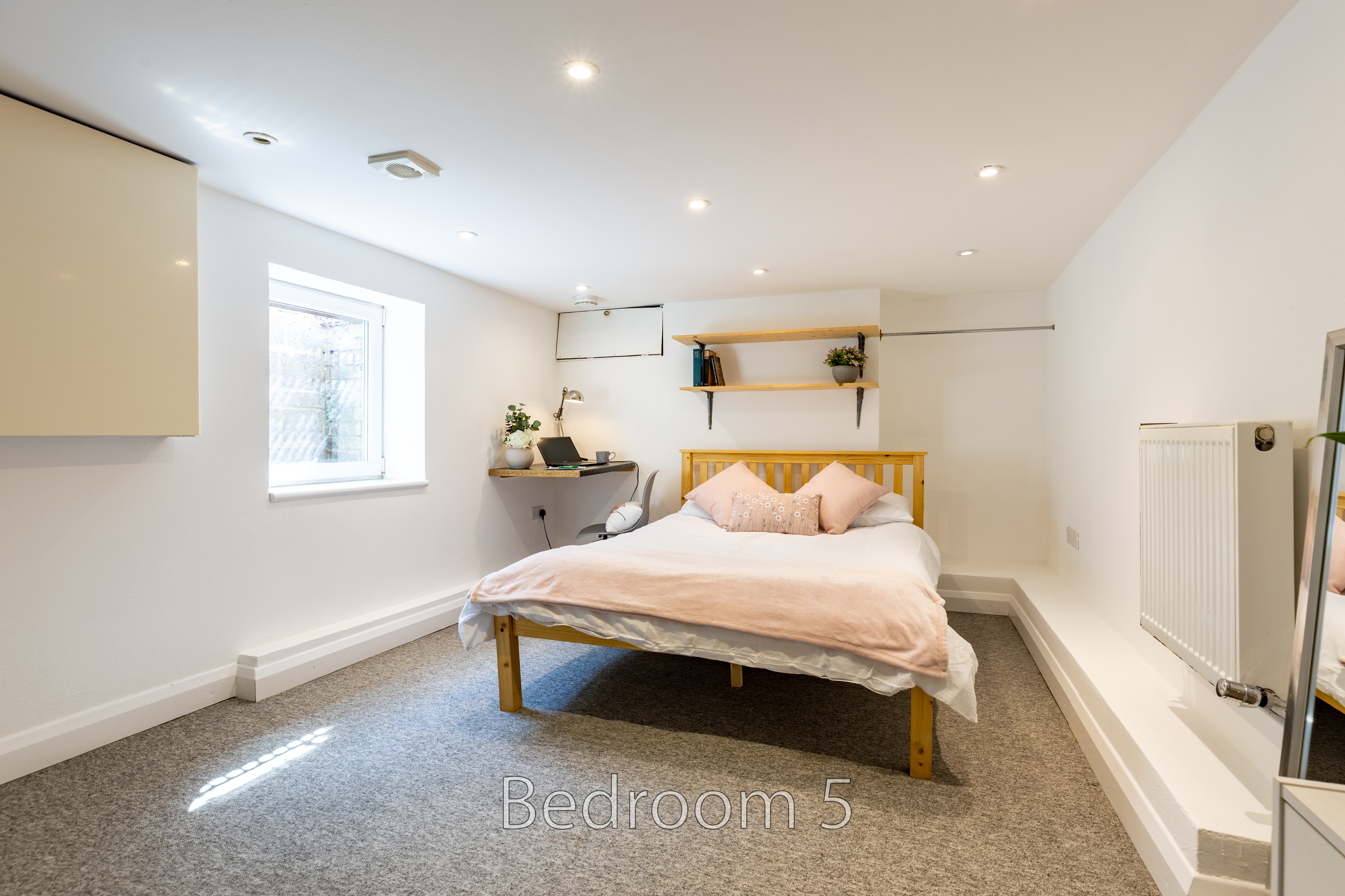 A furnished bedroom with a double bed, bedside table, shelves, radiator and window.