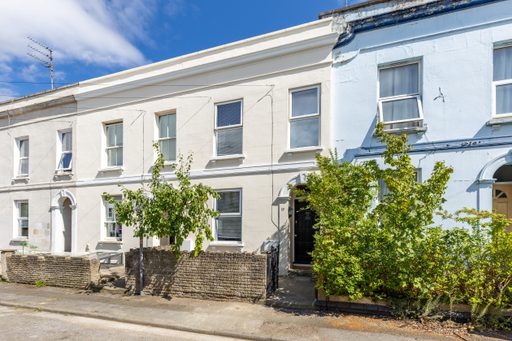 Row of attached terraced houses with pale façades, windows, front doors, small trees and low stone walls.