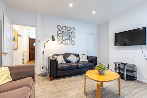 Bright living room with sofas, a round wooden coffee table, wall-mounted television, floor lamp and decorative wall mirror.