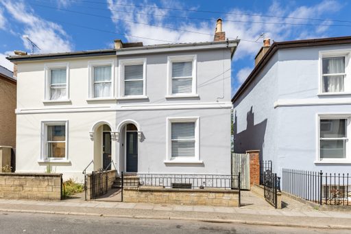 Front exterior of a white terraced house with two entrances, windows, railings and a small paved frontage.