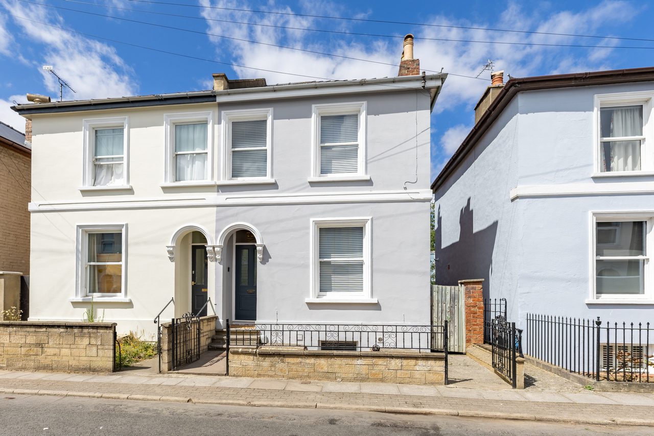 Front exterior of a white terraced house with two entrances, windows, railings and a small paved frontage.