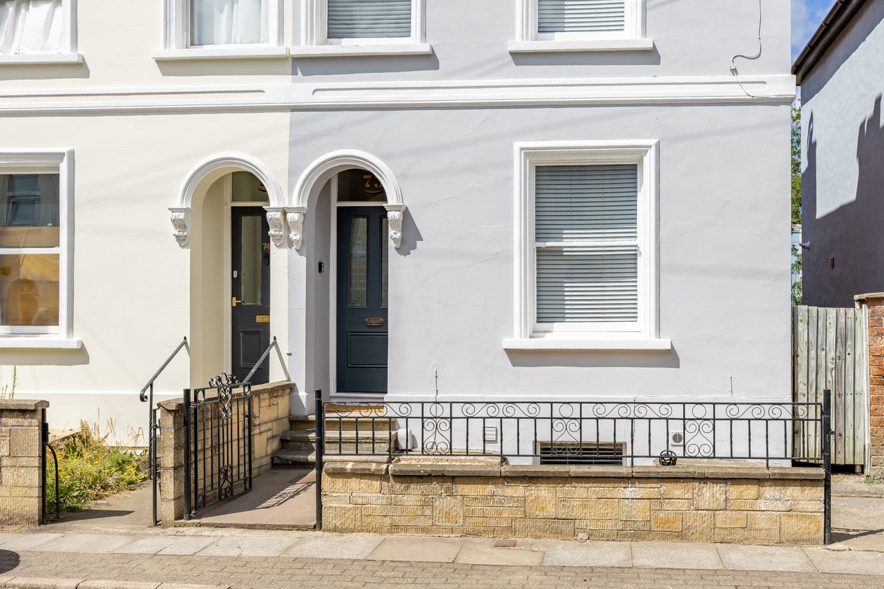 Front exterior of a terraced house with two arched entrances, windows, steps and a small paved forecourt.