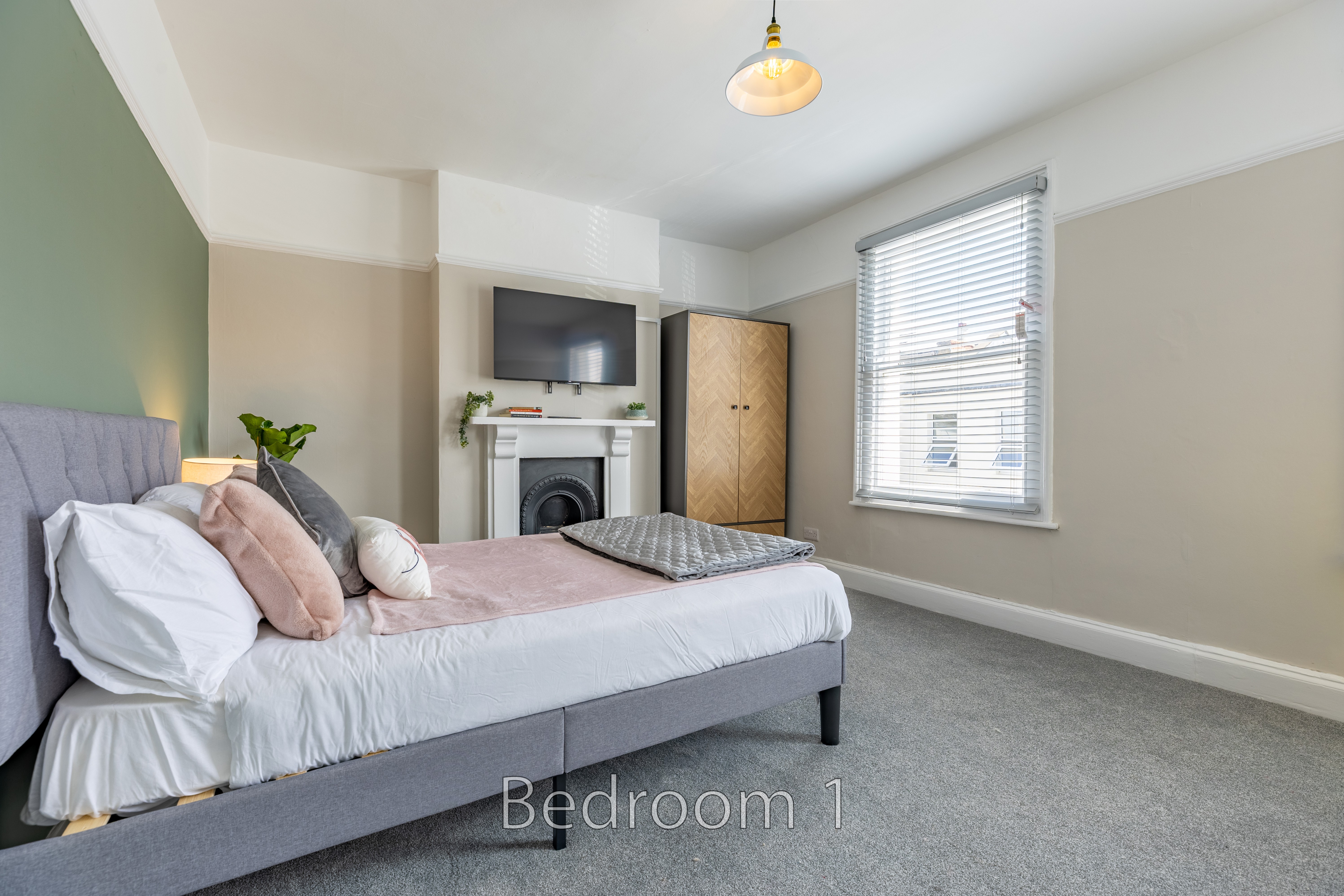 A furnished bedroom with a double bed, fireplace, television, wardrobe, window and carpeted floor.