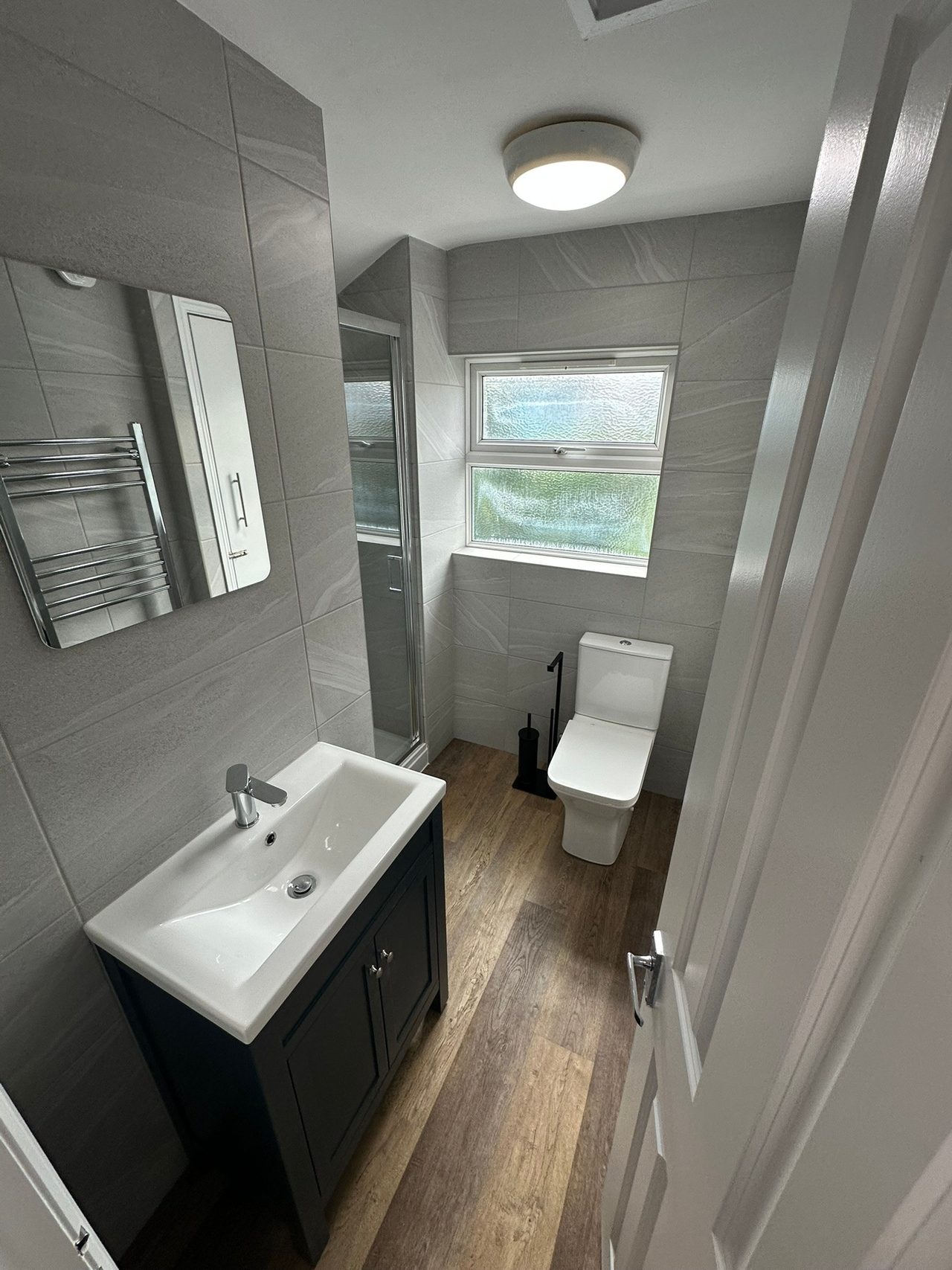 A small bathroom with a sink, toilet, shower enclosure, heated towel rail and frosted window.