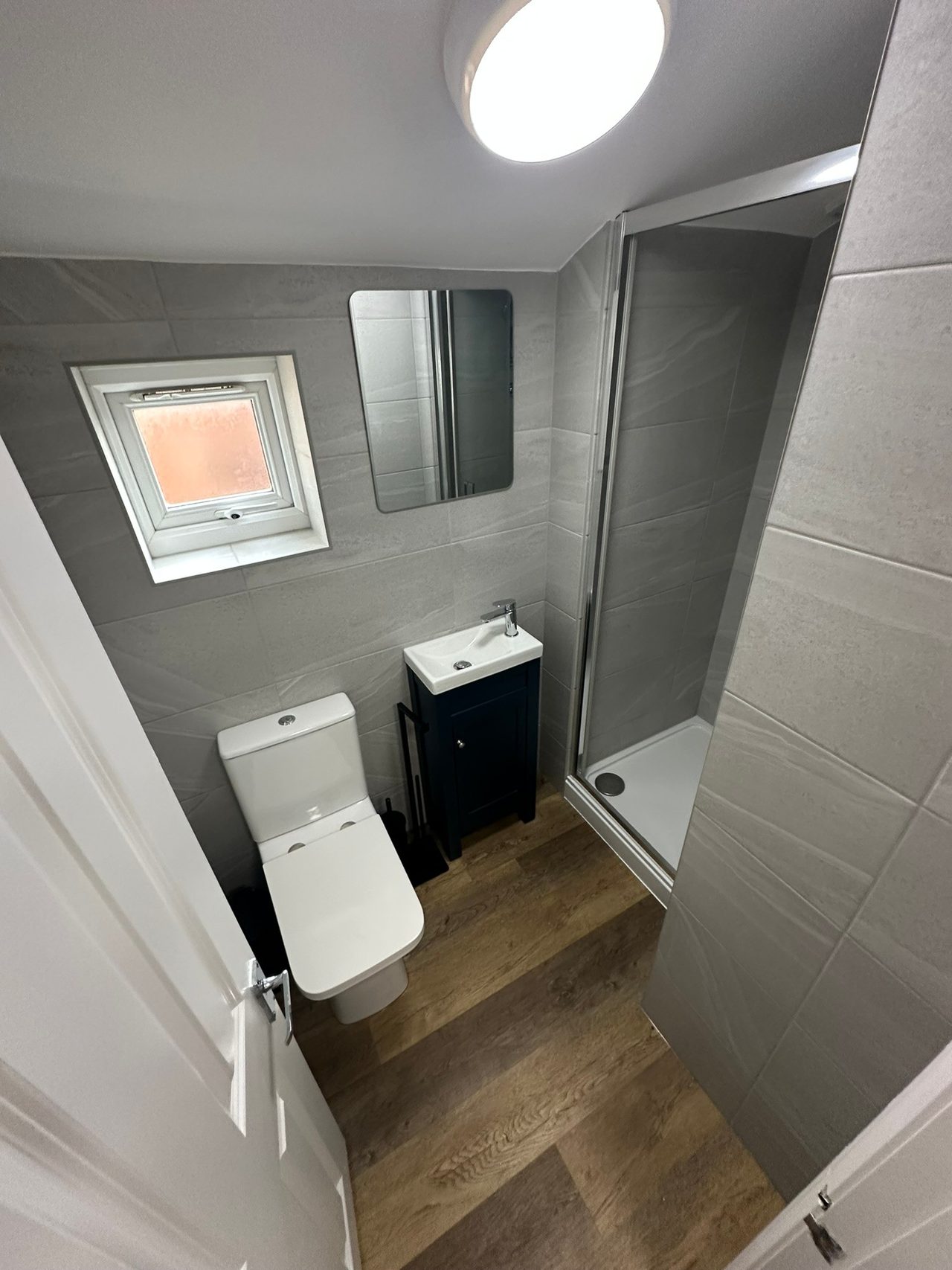 A compact tiled bathroom with a toilet, sink and glass shower enclosure.