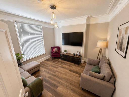 Furnished living room with sofas, an armchair, television, window blinds and wood-effect flooring.