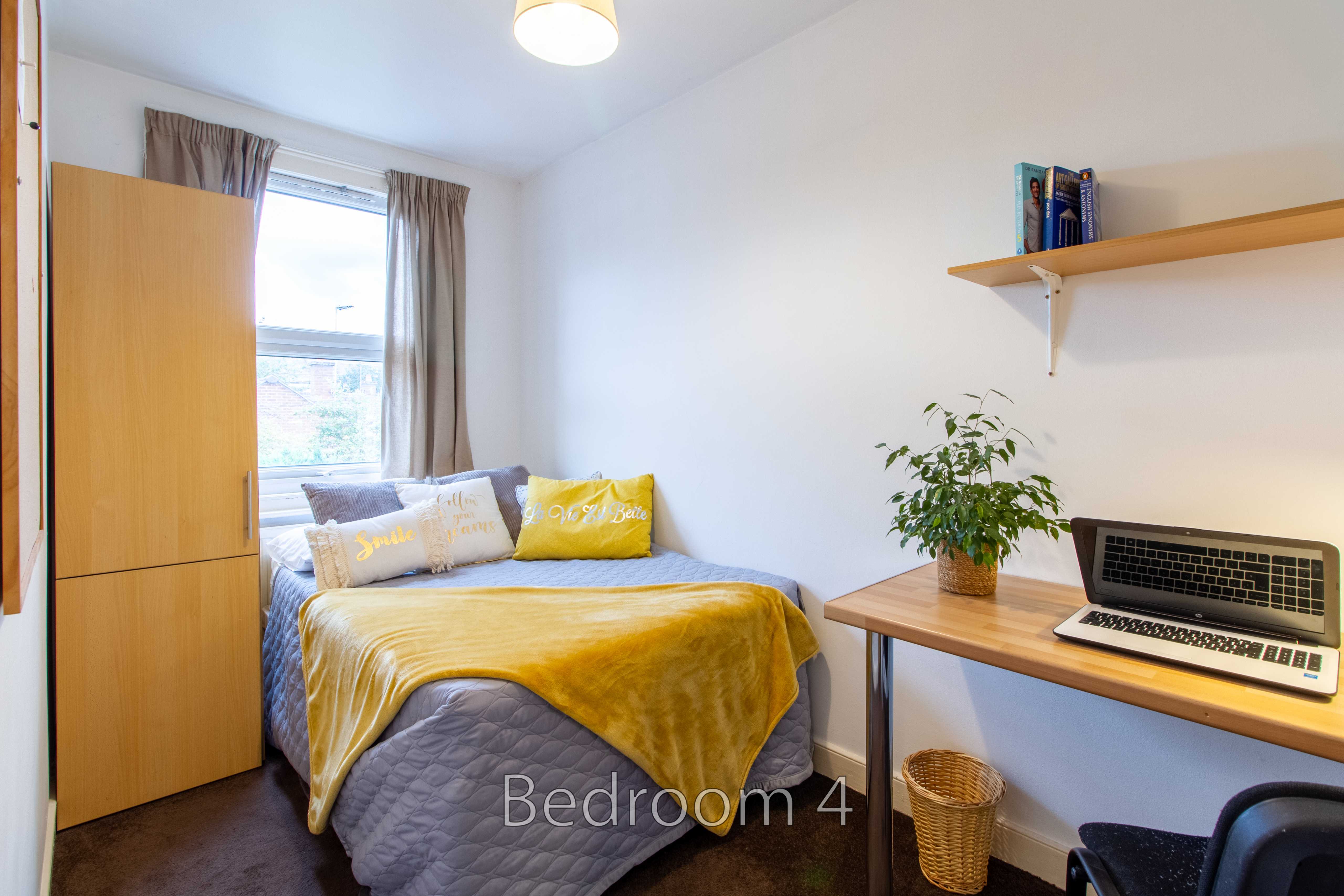 A furnished bedroom with a double bed, wardrobe, desk, chair, window and wall shelf.