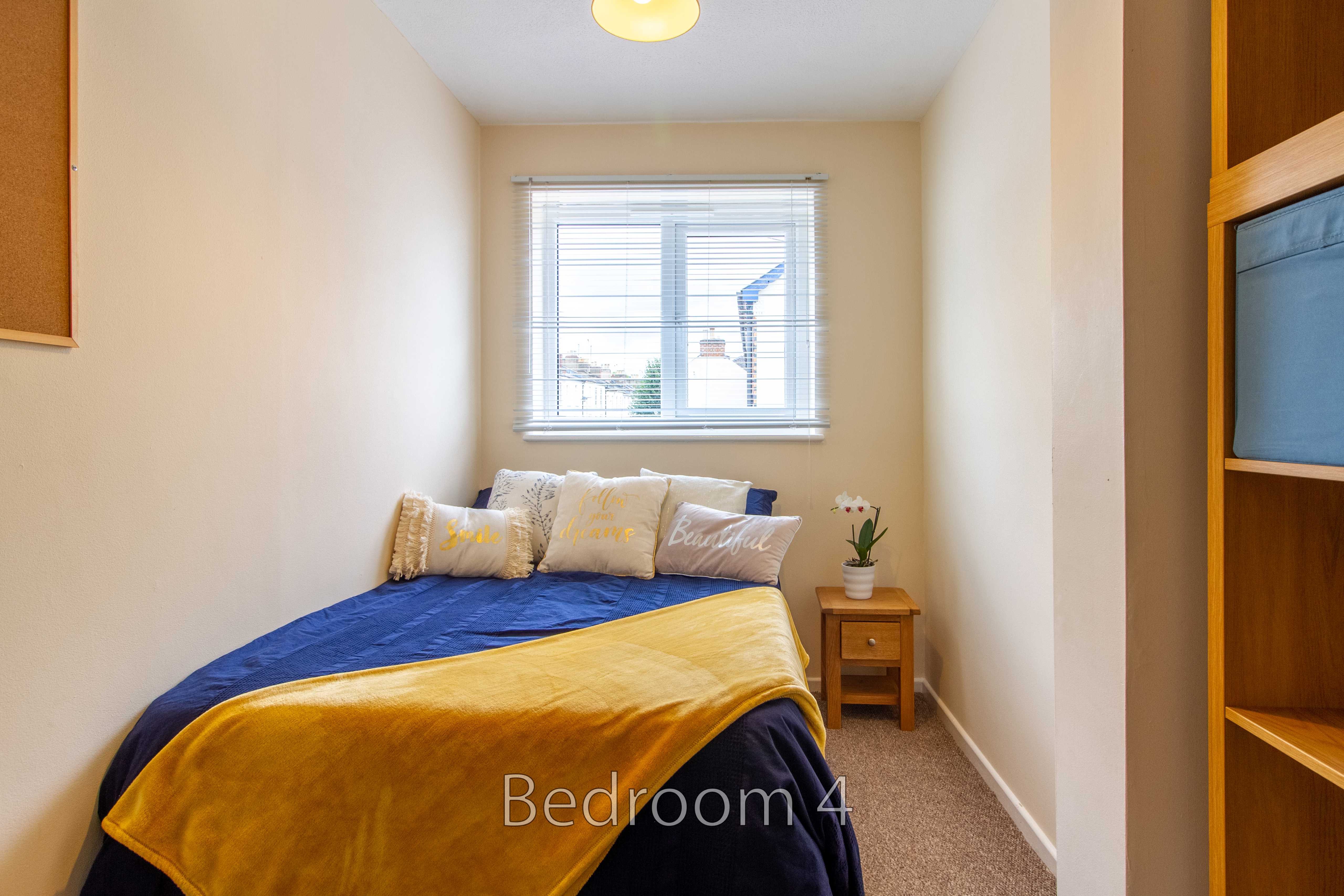 A small bedroom with a bed, window, bedside table and shelving.