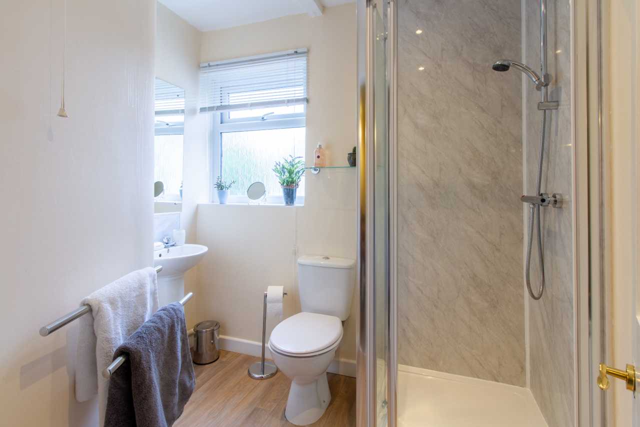 A bright bathroom with a toilet, pedestal sink, towel rail, and glass-enclosed shower.