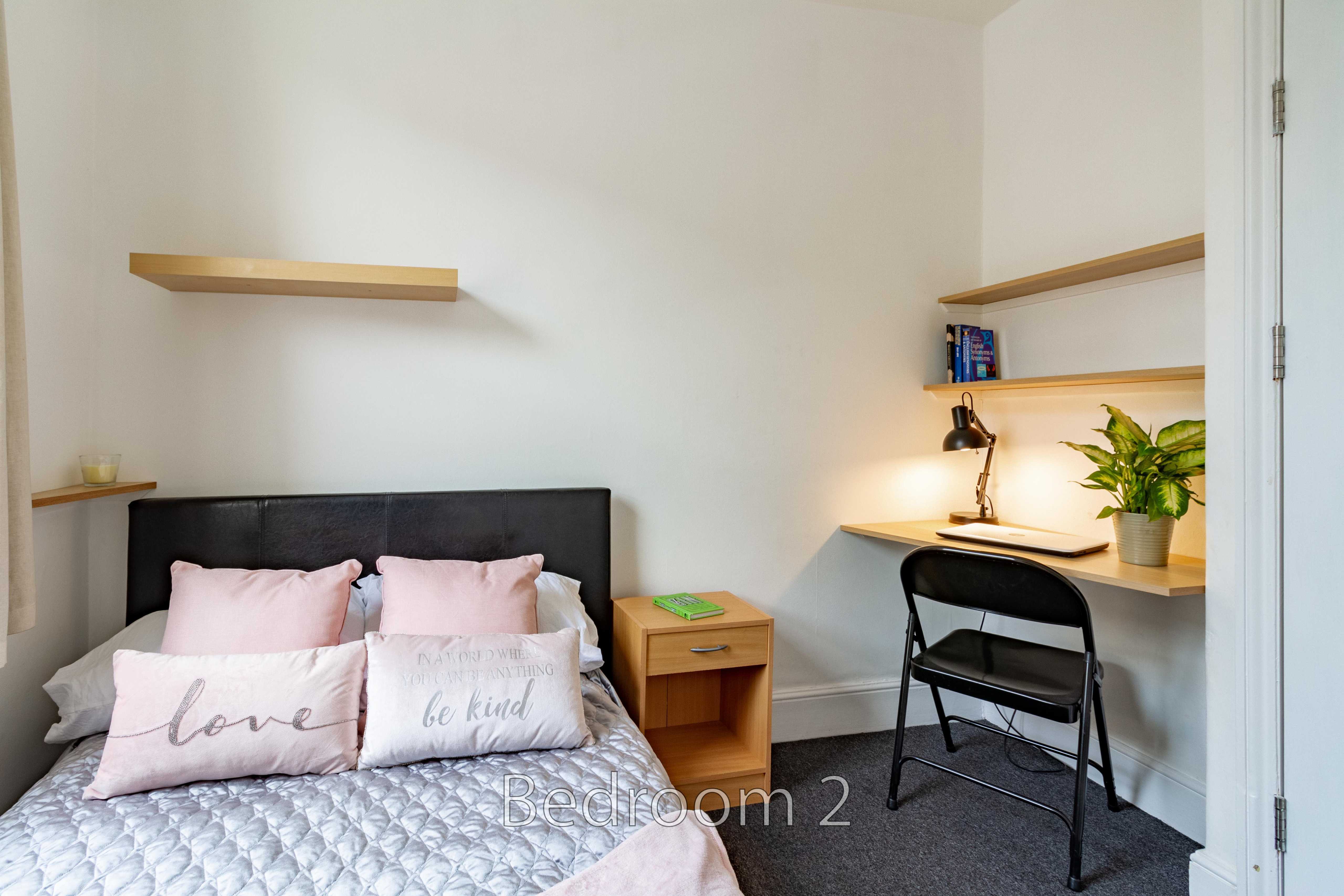A bedroom with a double bed, desk, chair, shelves and bedside table.