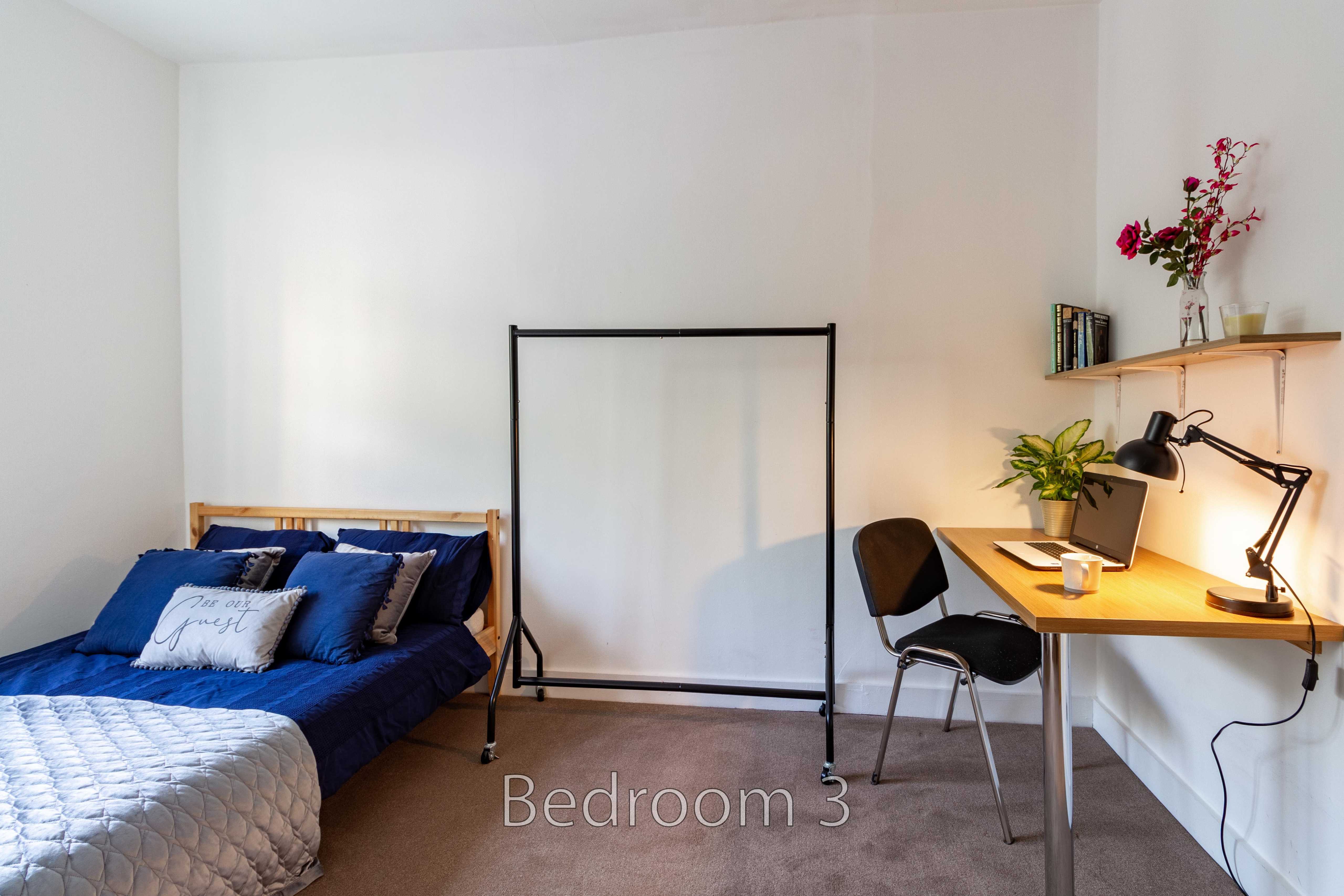 Bedroom with a bed, desk, chair, clothes rail and wall shelf.