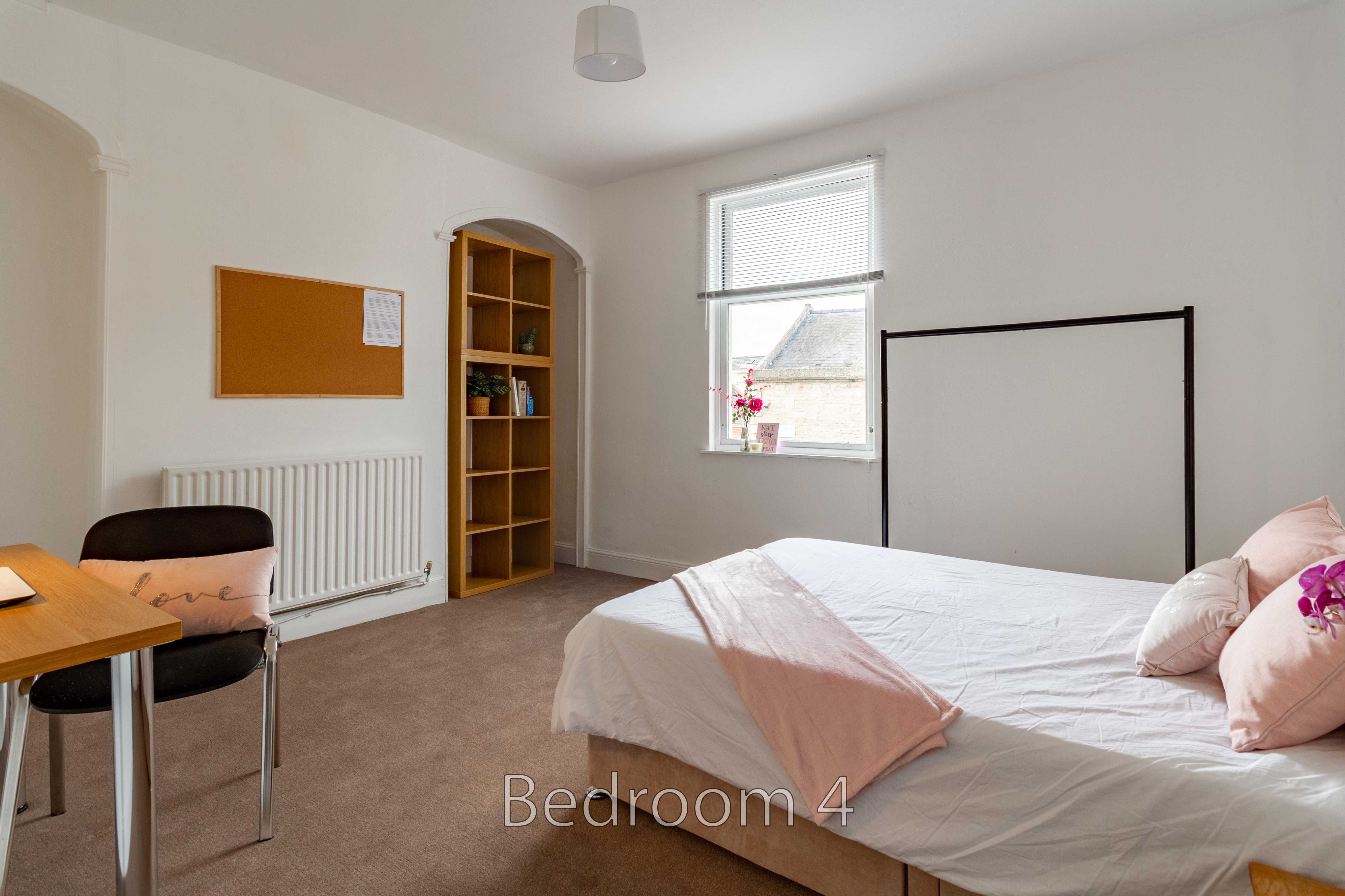 A bedroom with a double bed, desk, radiator, shelving and a window.