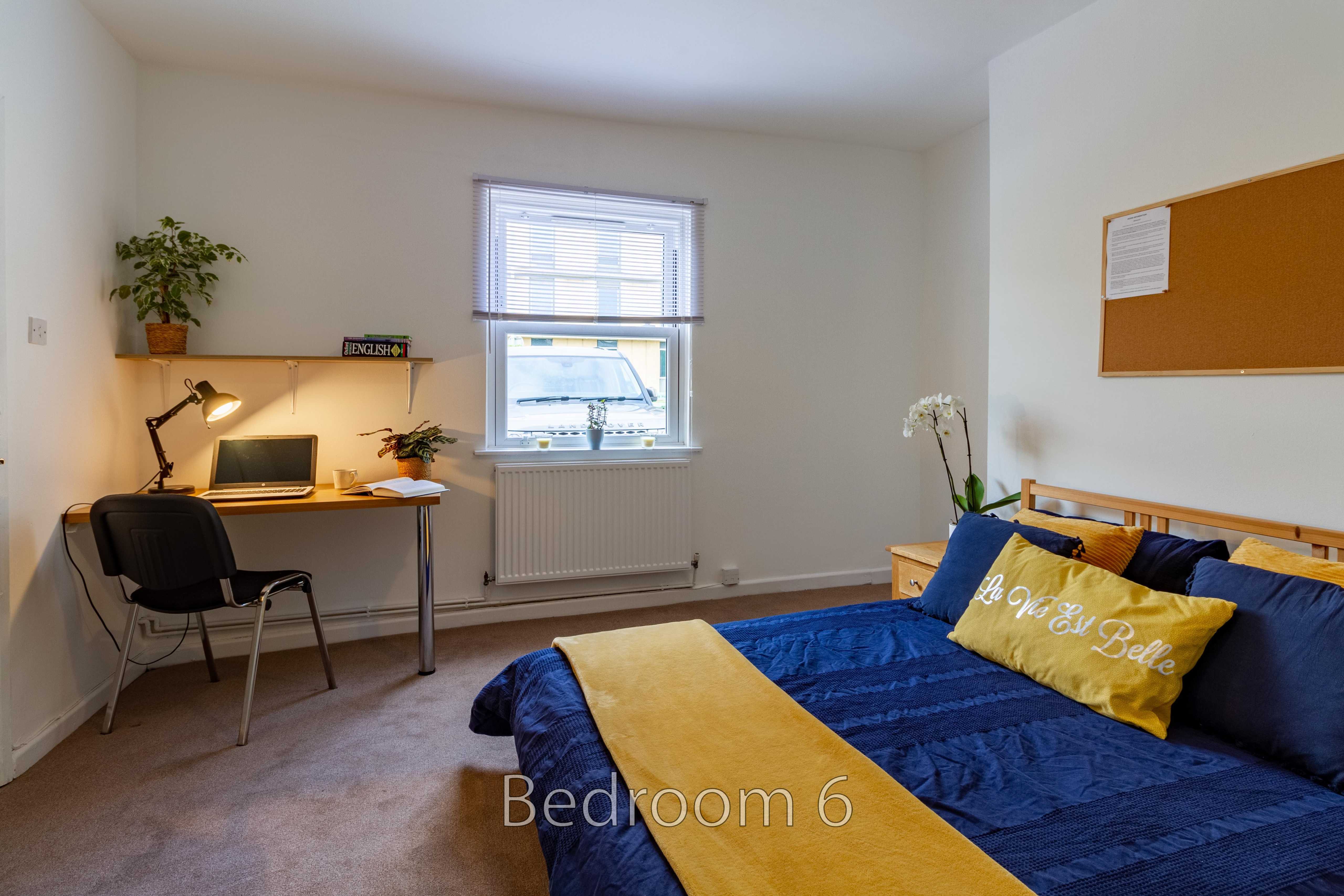 A furnished bedroom with a double bed, desk, chair, window and radiator.