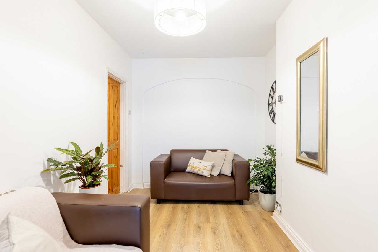 Bright furnished living area with two brown sofas, wood flooring, potted plants and a wall mirror.