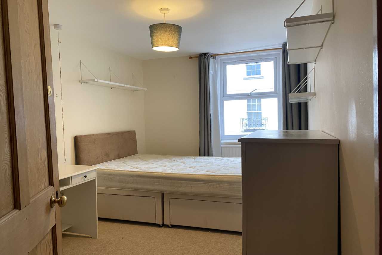 A small bedroom with a bed, wardrobe, shelving, pendant light and window.