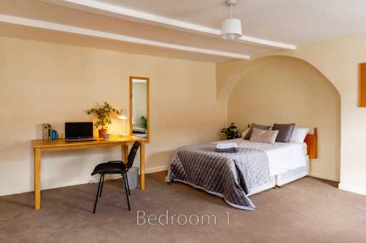 A bedroom with a double bed, desk, chair, lamp and television.