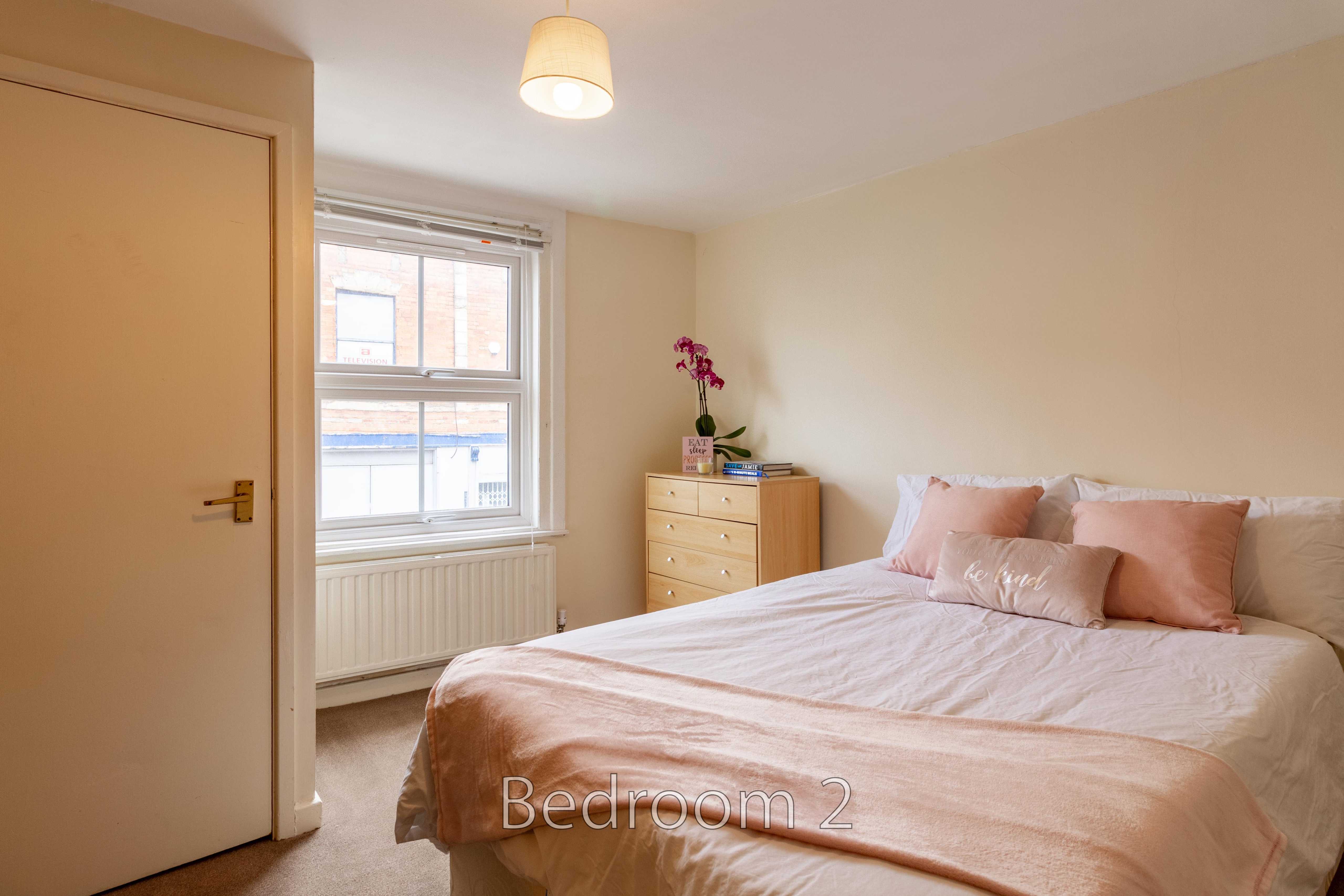 A furnished bedroom with a double bed, bedside pillows, chest of drawers, window and radiator.