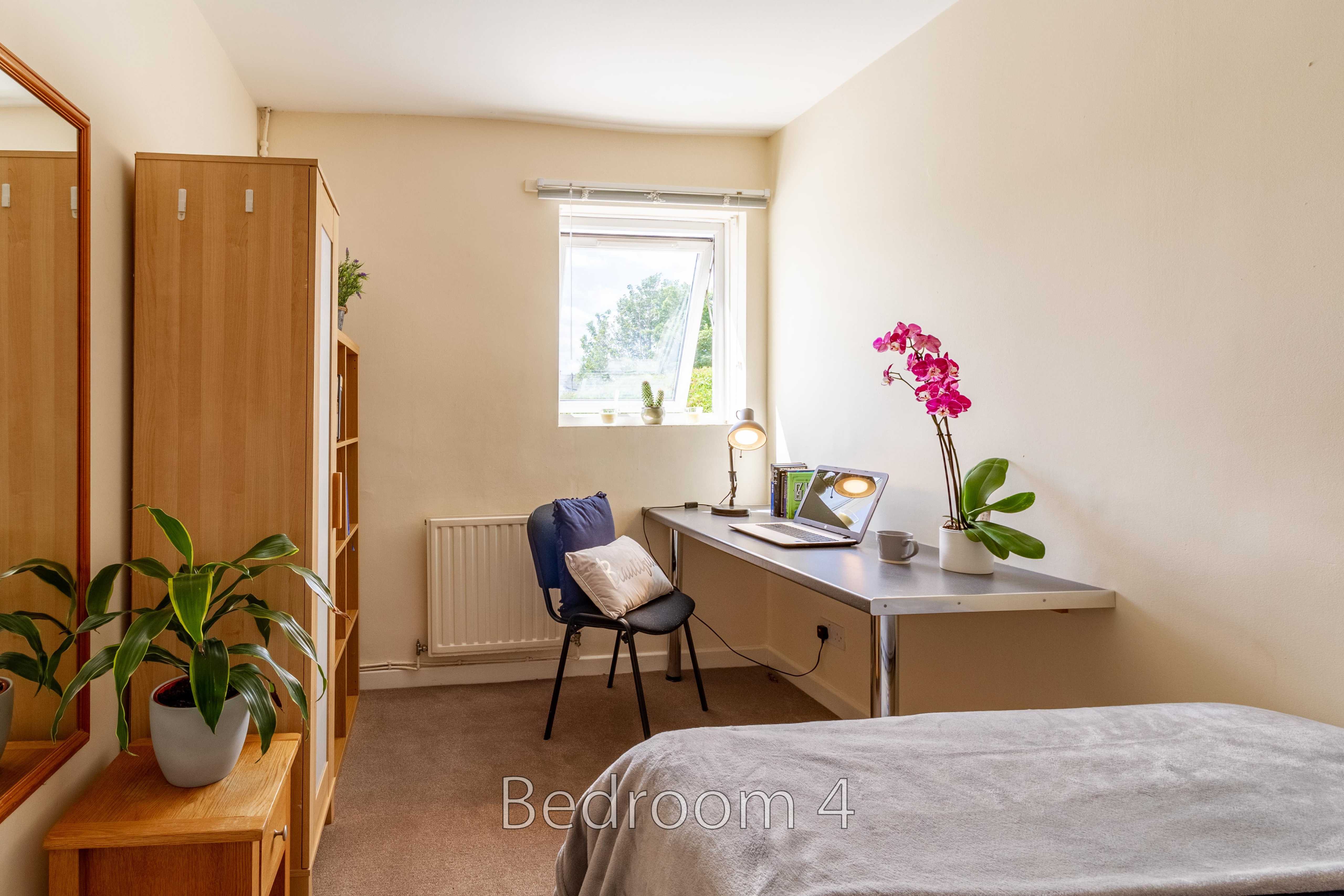 A bedroom with a bed, desk, chair, wardrobe, window and potted plants.