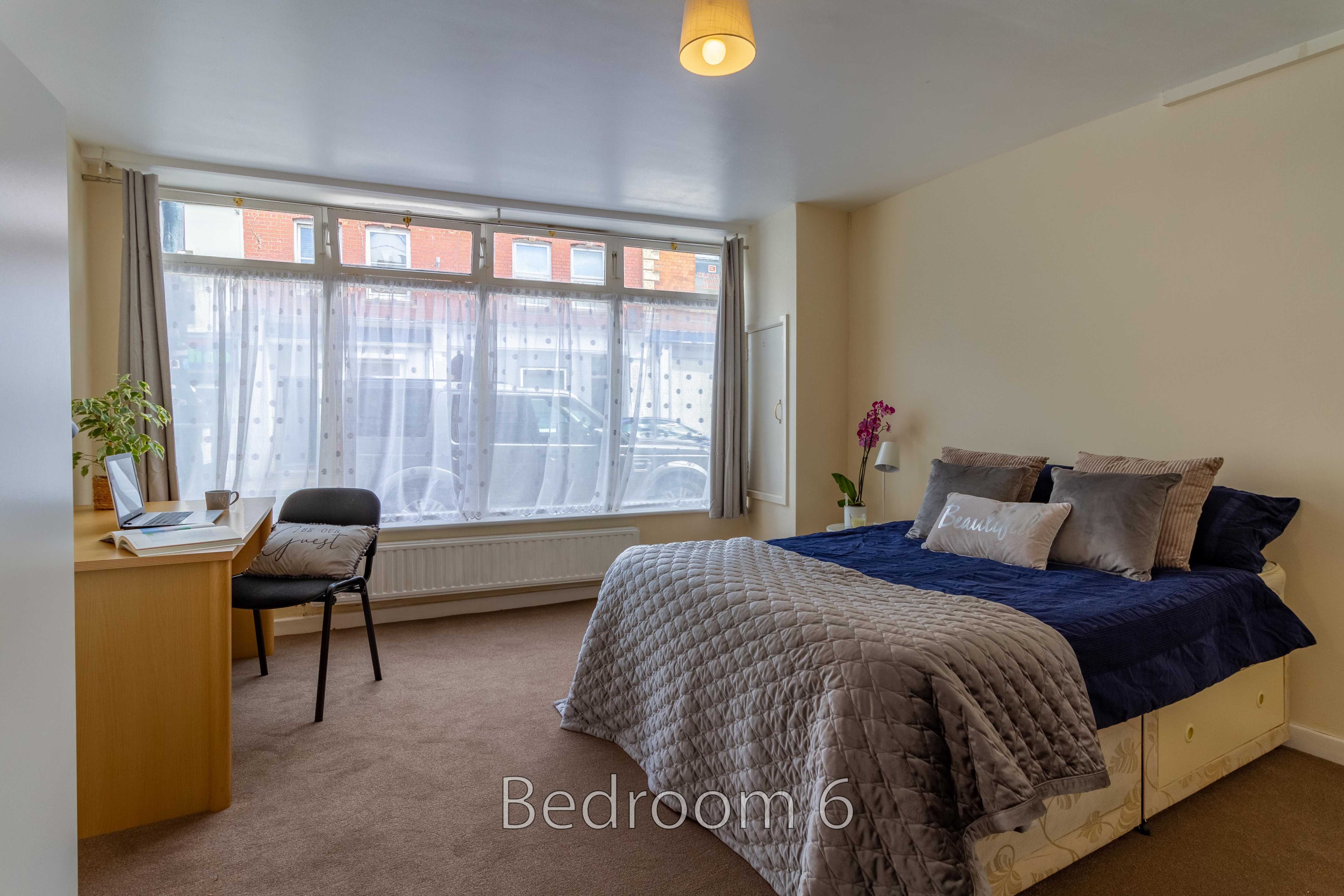 Furnished bedroom with a double bed, desk, chair, large window and radiator.