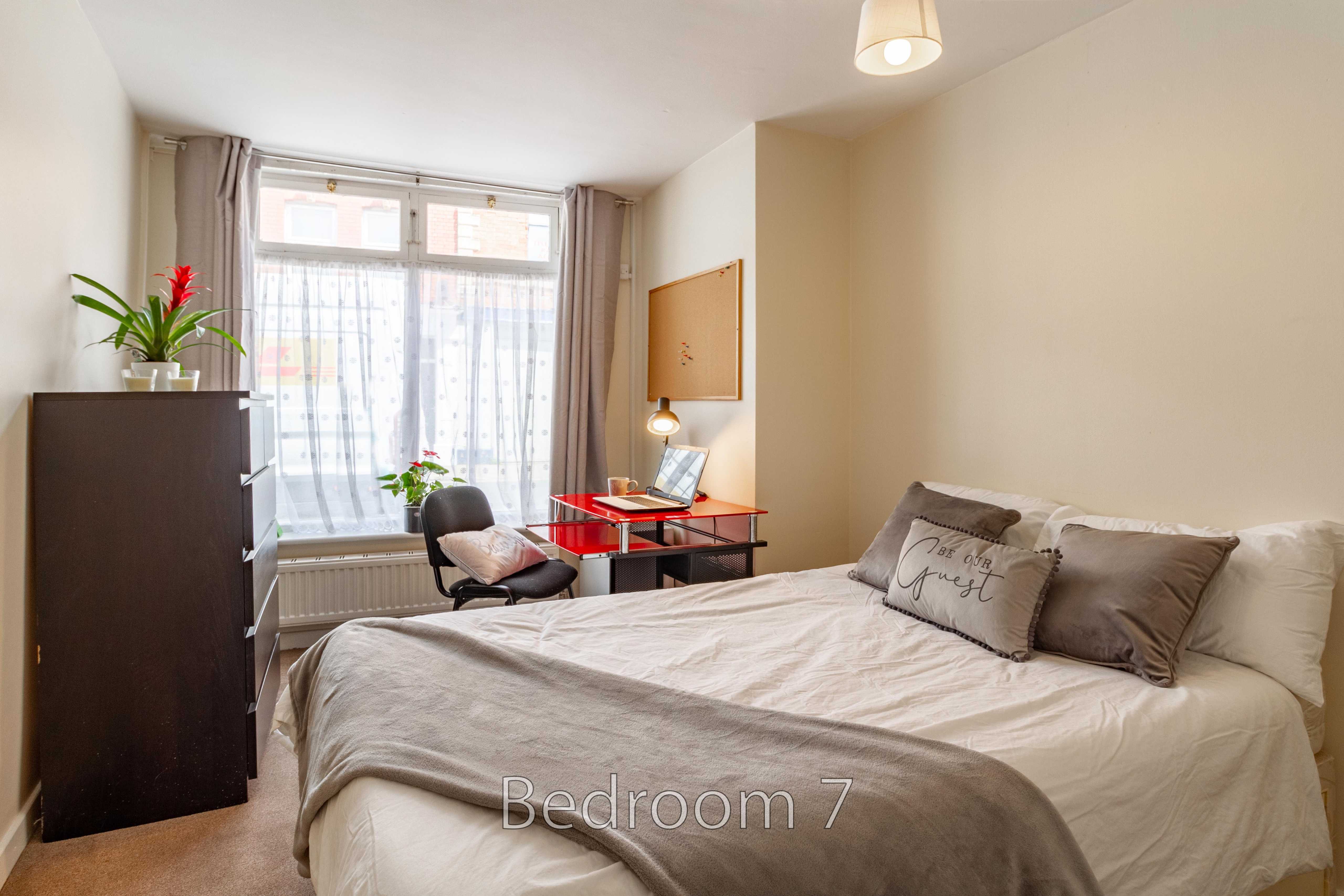 A furnished bedroom with a double bed, desk, chair, wardrobe, window and curtains.
