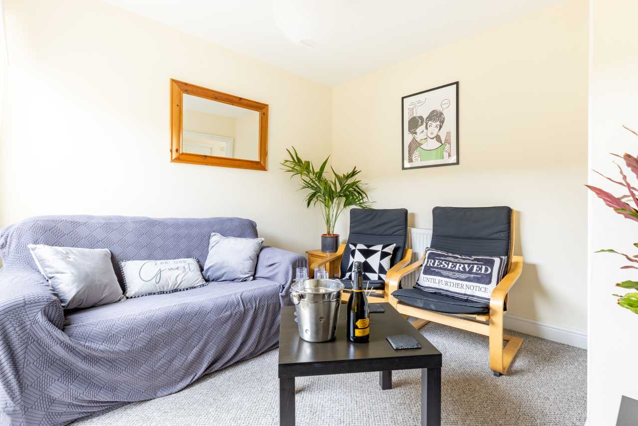 Bright shared lounge with a sofa, two chairs, a coffee table, plants and framed artwork.