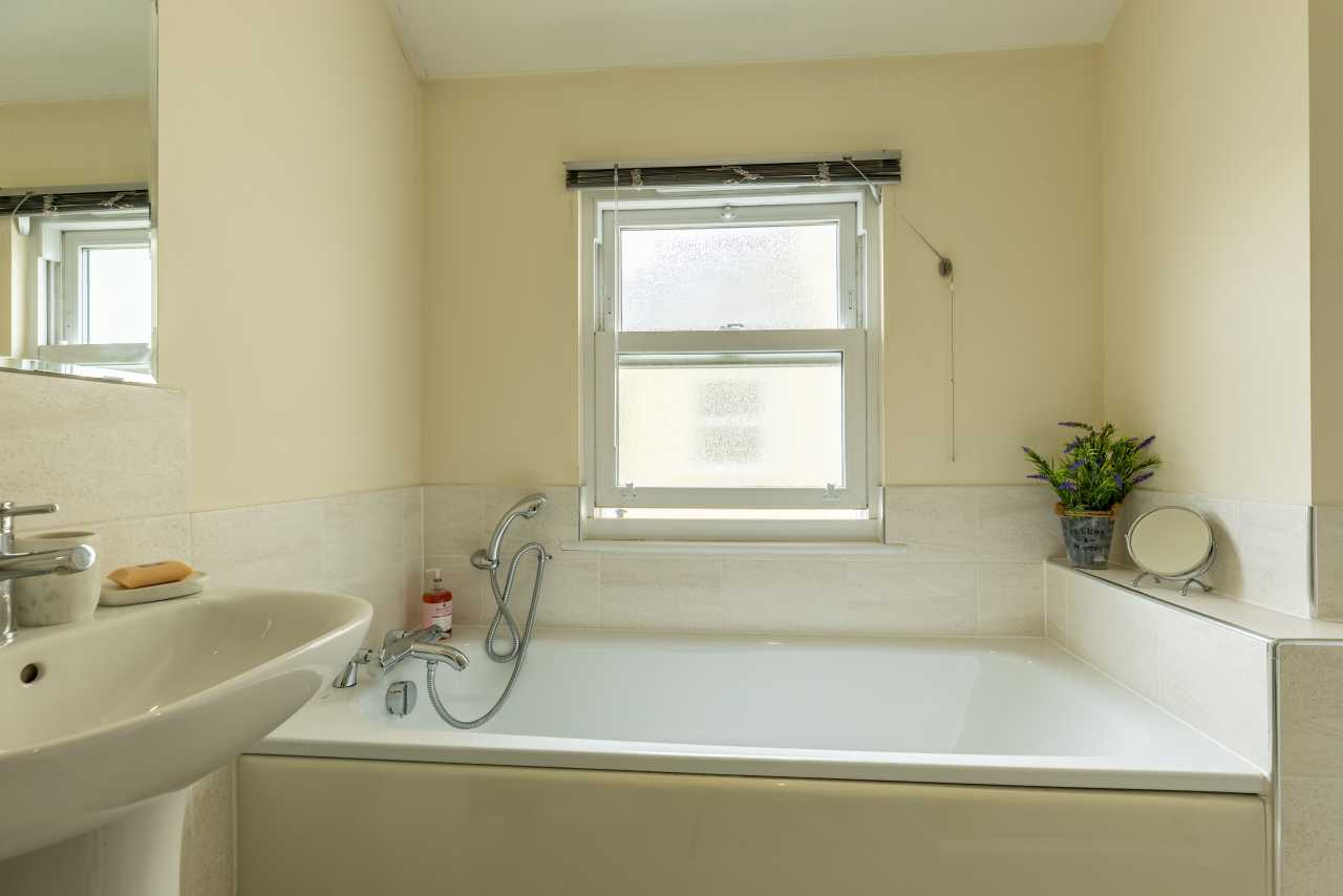 Bathroom with a bathtub, sink, tiled walls, frosted window and small potted plant.