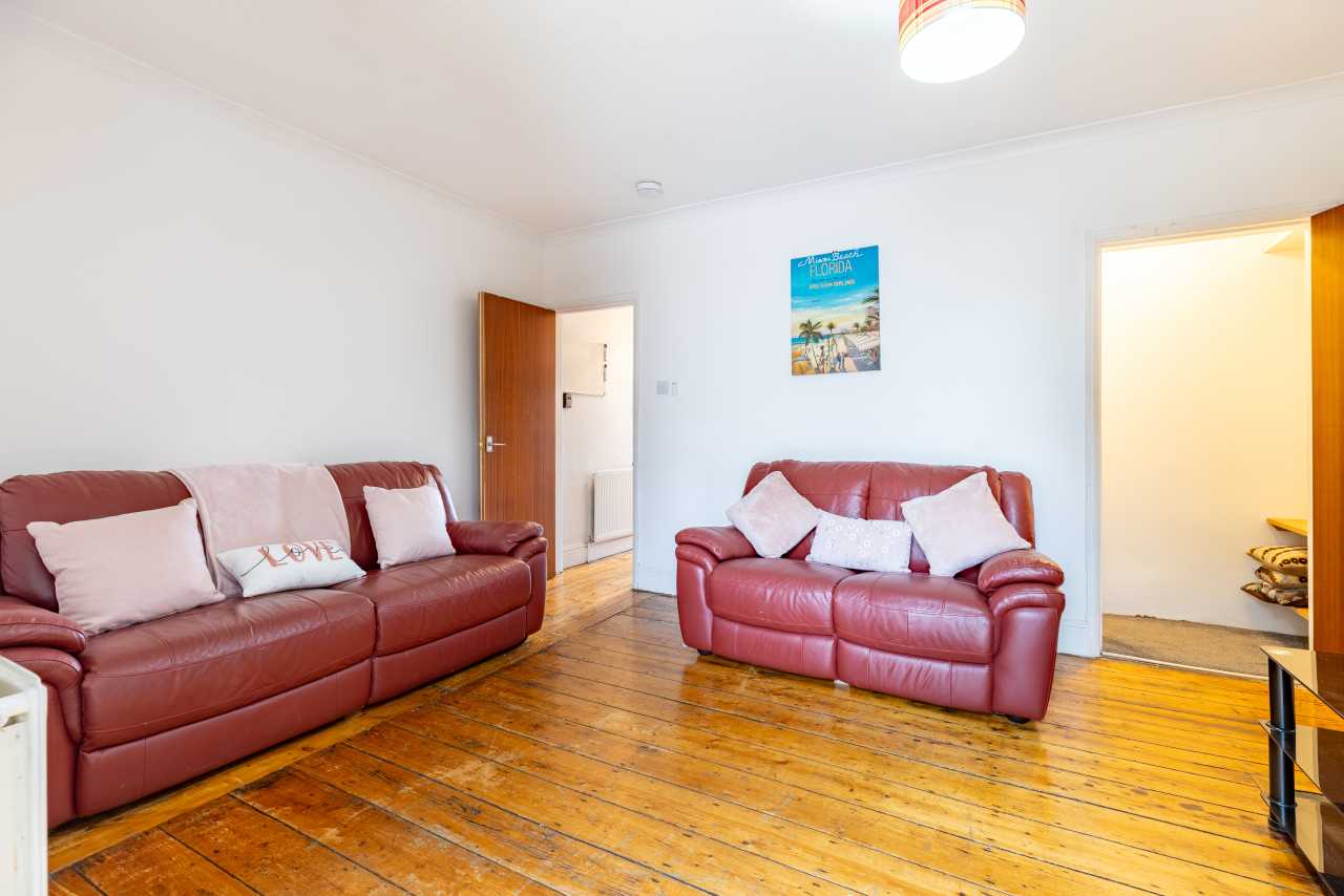 Living room with red leather sofas, wooden flooring, white walls and two open doorways.