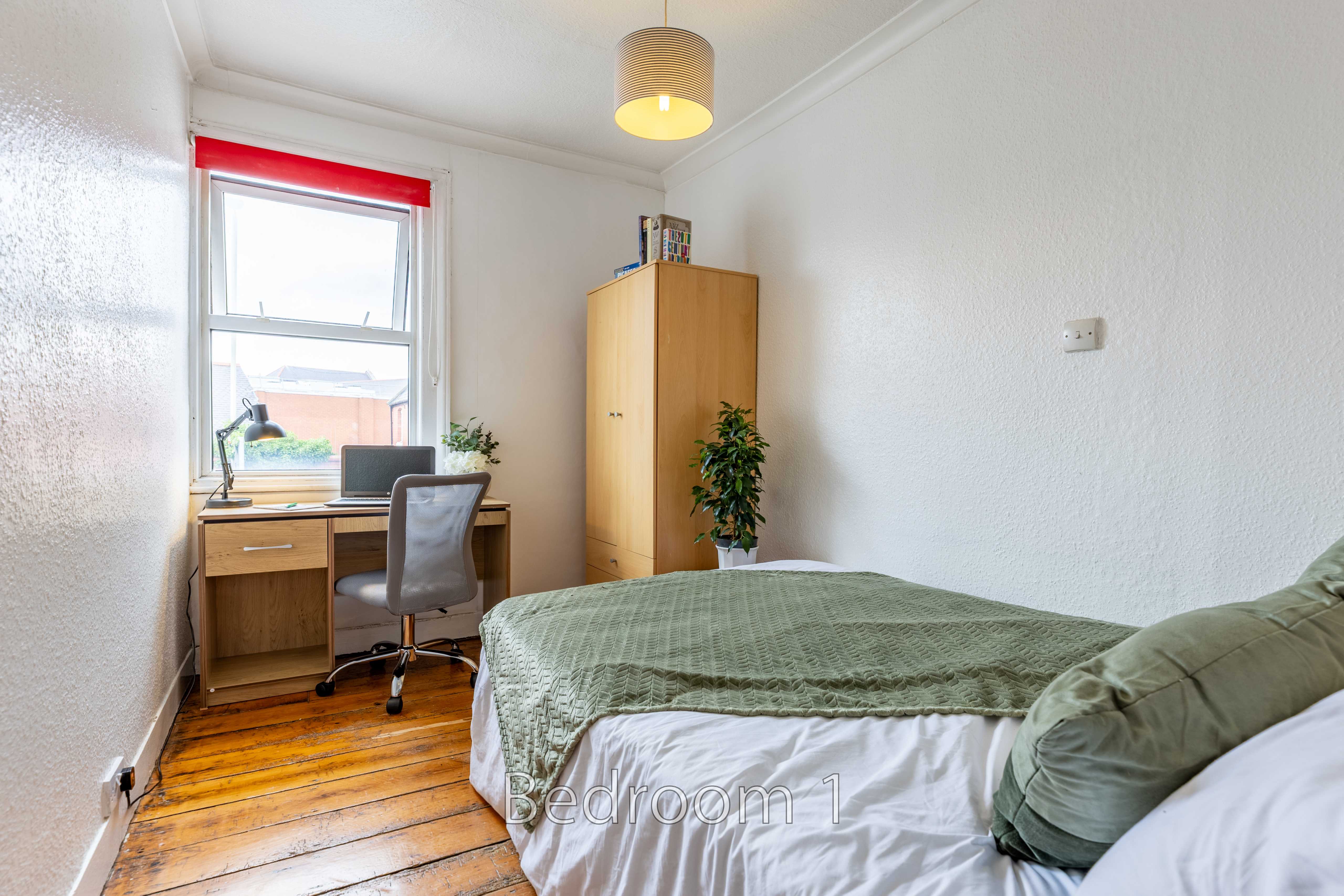 A bedroom with a bed, desk, chair, wardrobe, window and wooden floor.