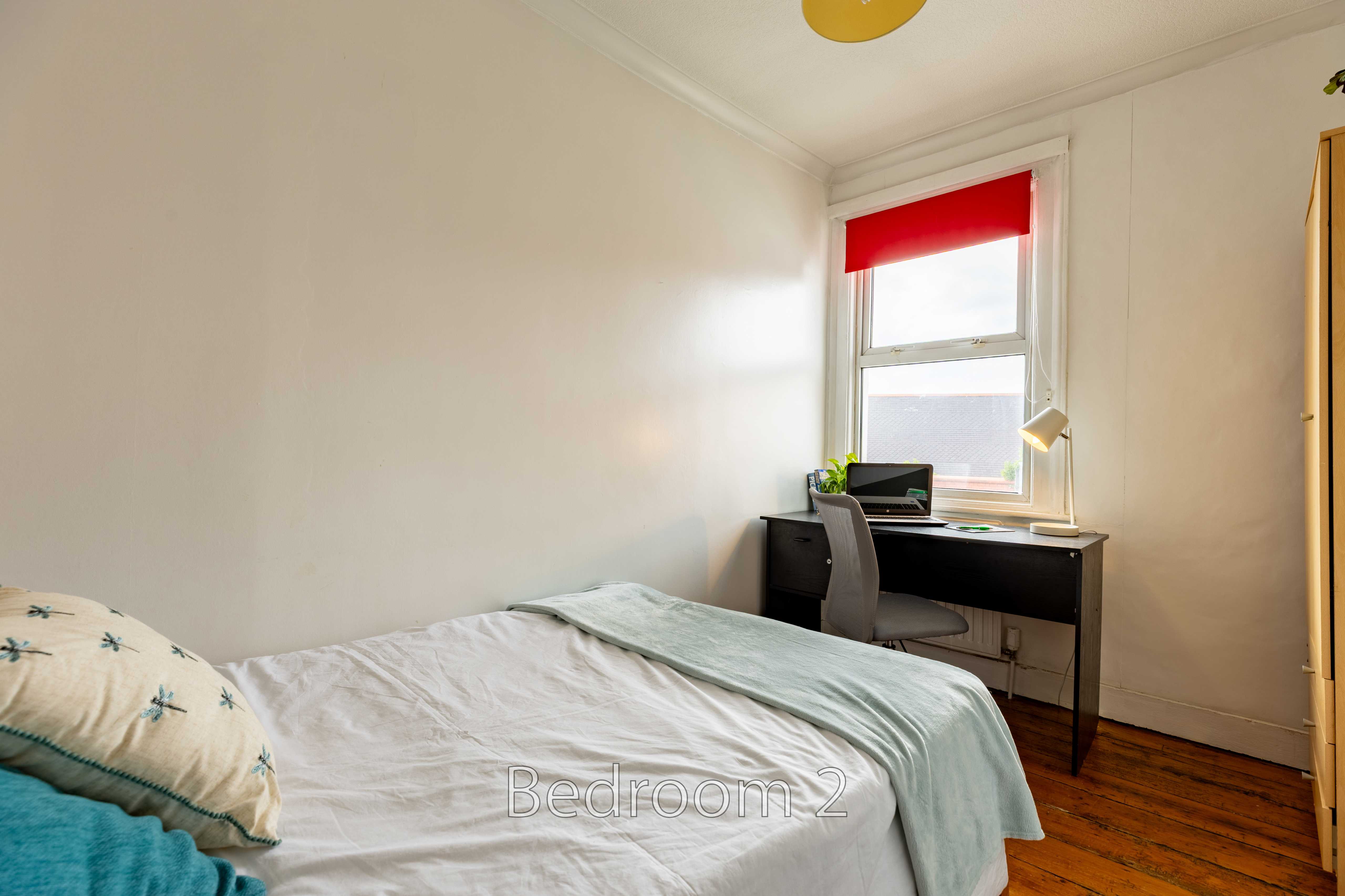 A bedroom with a bed, desk, chair, wardrobe and window.