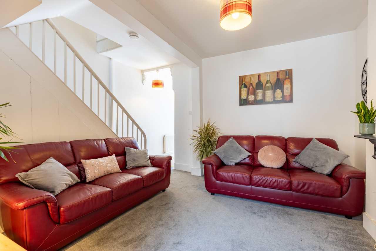 A shared lounge with two red leather sofas, cushions, a carpet, plants, wall art and a staircase.