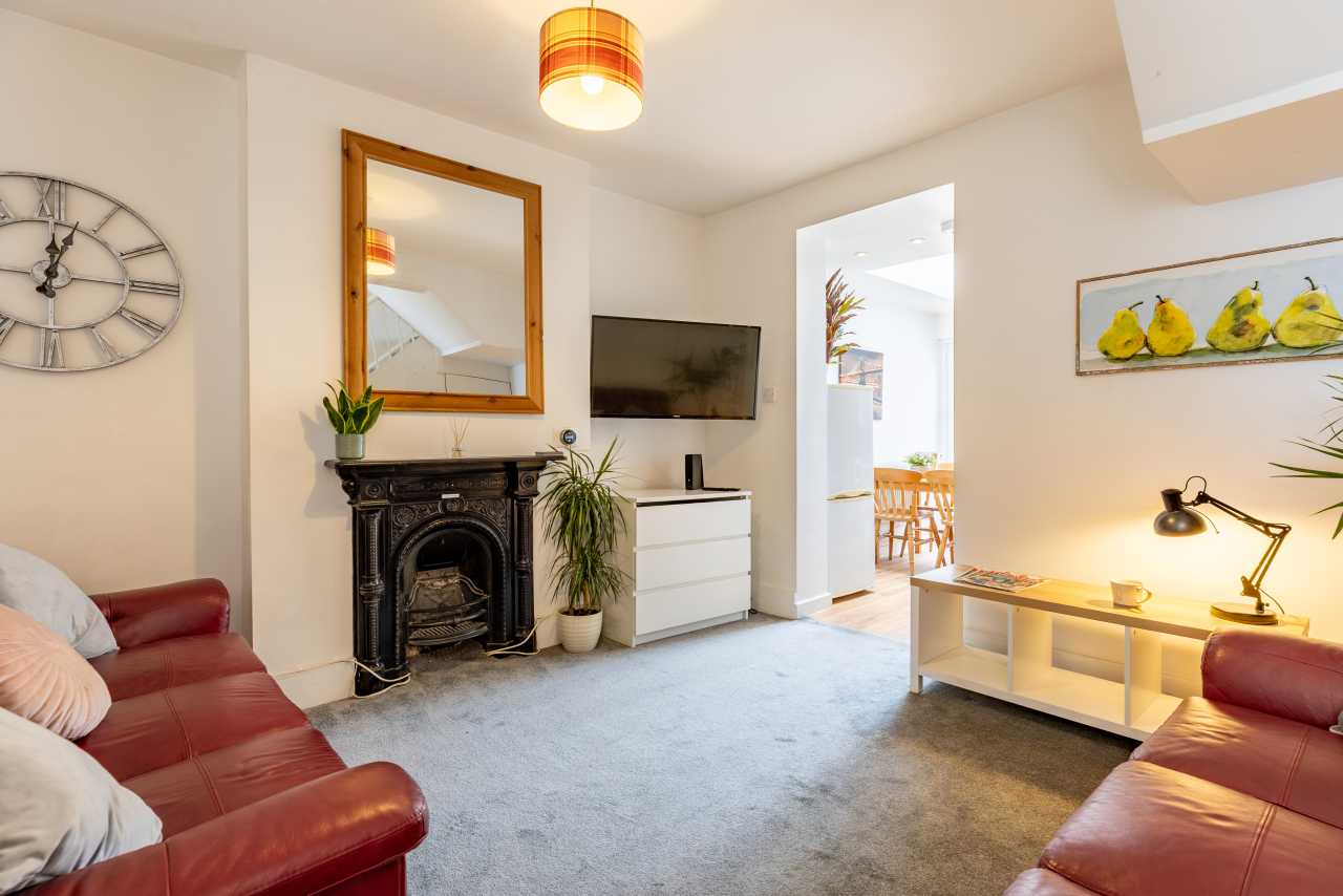 A furnished living room with red sofas, a decorative fireplace, television, cabinet, coffee table and doorway to a dining area.