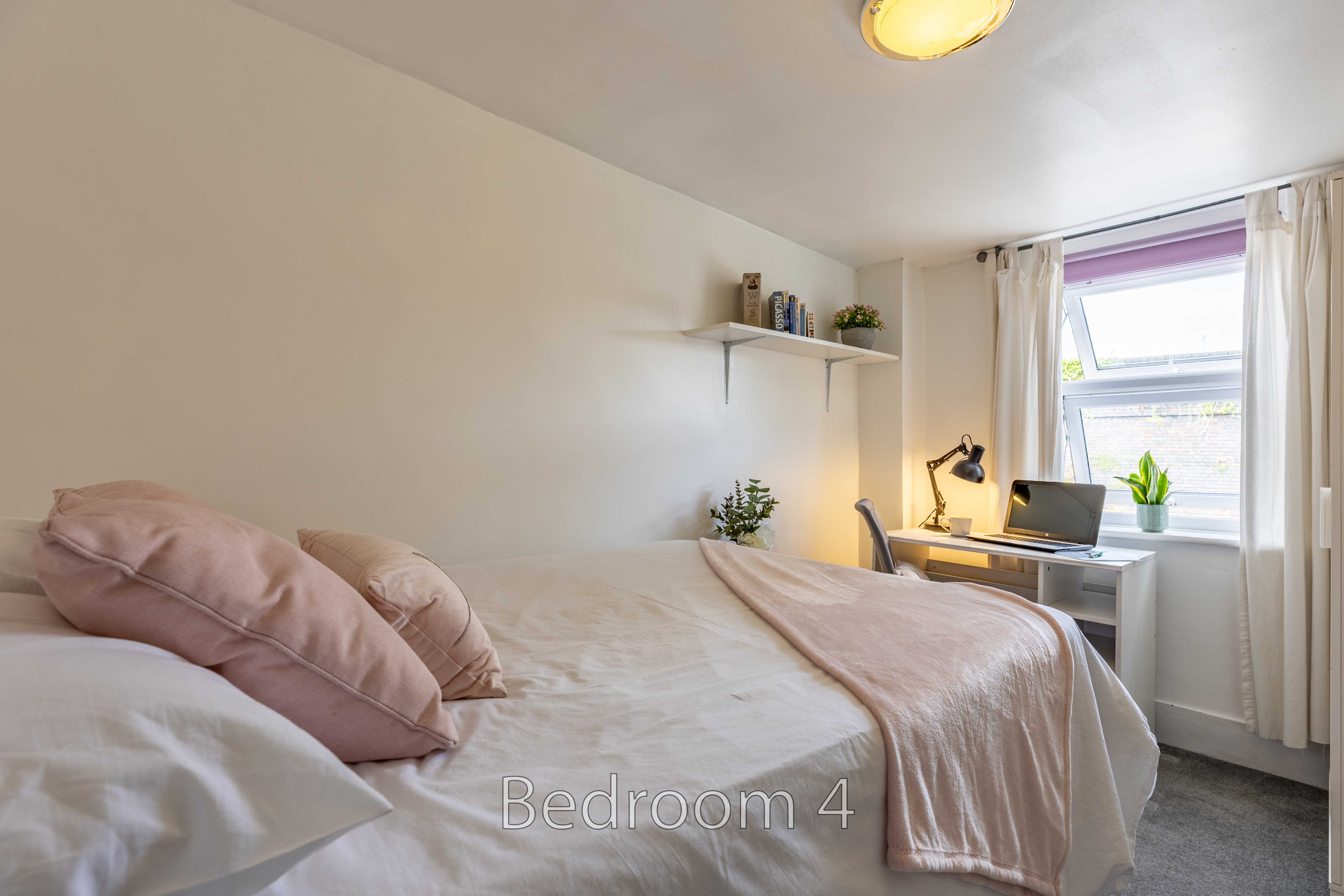 A furnished bedroom with a double bed, desk, window and shelving.