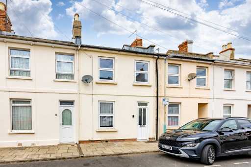 Row of attached terraced houses with front doors, windows, chimneys and parked cars along the street.