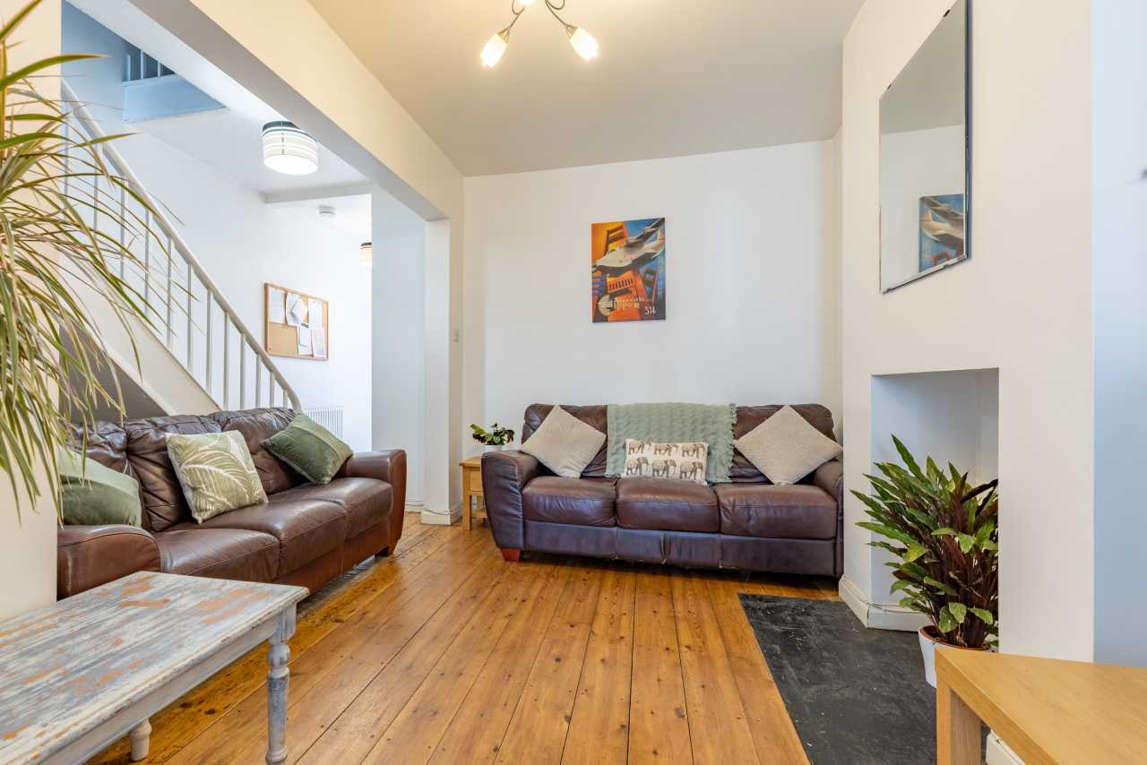 Bright shared living area with two leather sofas, wooden flooring, artwork, plants and a staircase.